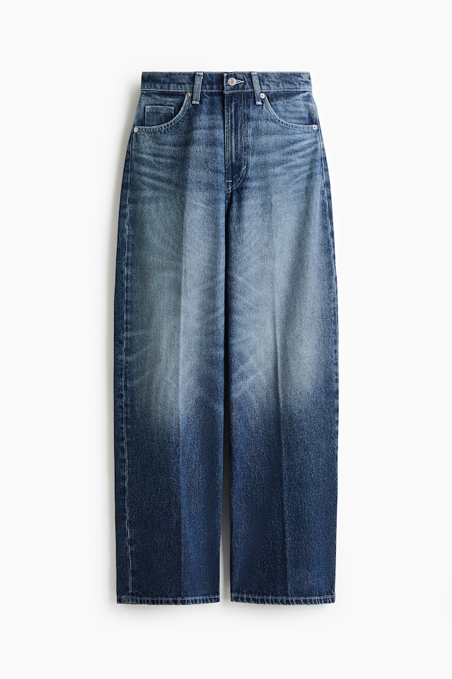 These blue denim jeans are shown facing front, featuring a loose, wide-leg fit with sharp pressed creases running down the center of each leg. The jeans are displaying a faded, whiskered wash across the lap and thighs, a classic five-pocket construction, and a regular waist with a button closure. - 1