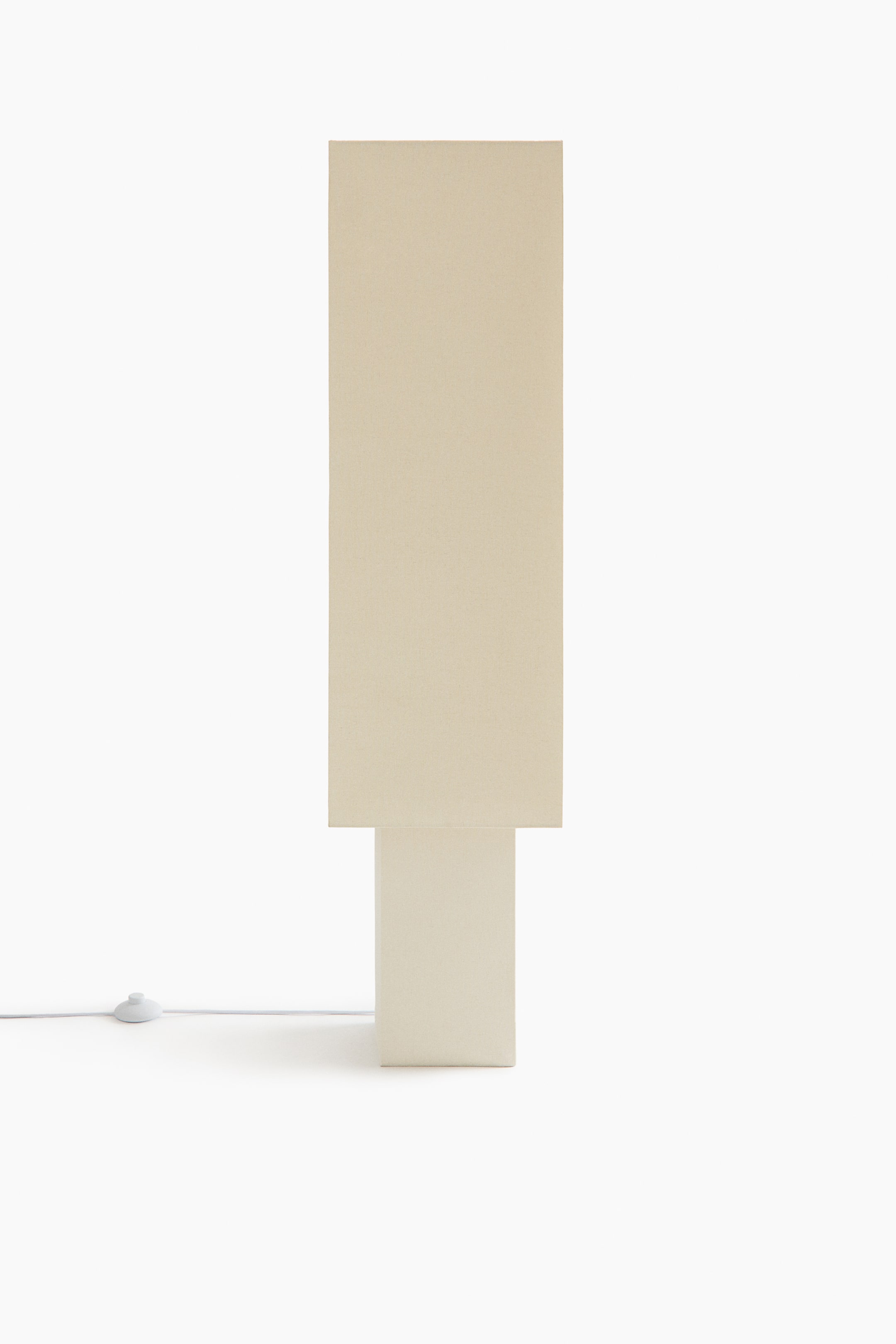Agrandir l'image: La lampe présente un abat-jour rectangulaire haut de couleur beige clair, reposant sur une base rectangulaire plus basse. Un cordon d’alimentation blanc avec interrupteur intégré sort de la base.