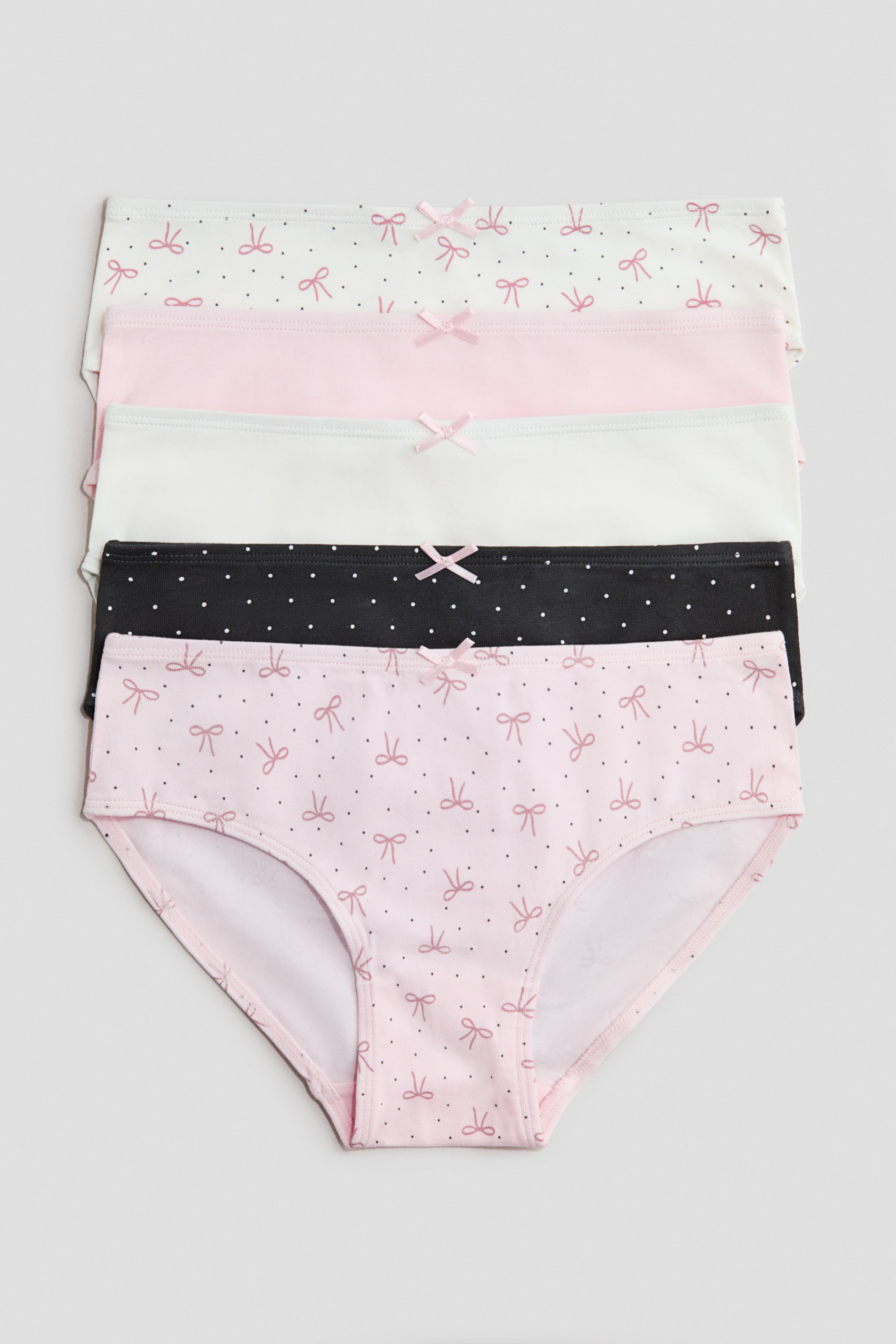 Xem ảnh lớn hơn: Một chồng gồm năm chiếc quần lót cotton jersey trưng bày nhiều màu sắc và họa tiết khác nhau, tất cả đều hướng mặt trước. Mỗi chiếc đều có một chiếc nơ trang trí nhỏ ở chính giữa phần cạp trước. Chiếc ở dưới cùng, mang họa tiết nơ và chấm bi màu hồng nhạt, đồng thời để lộ phần đáy có lót.