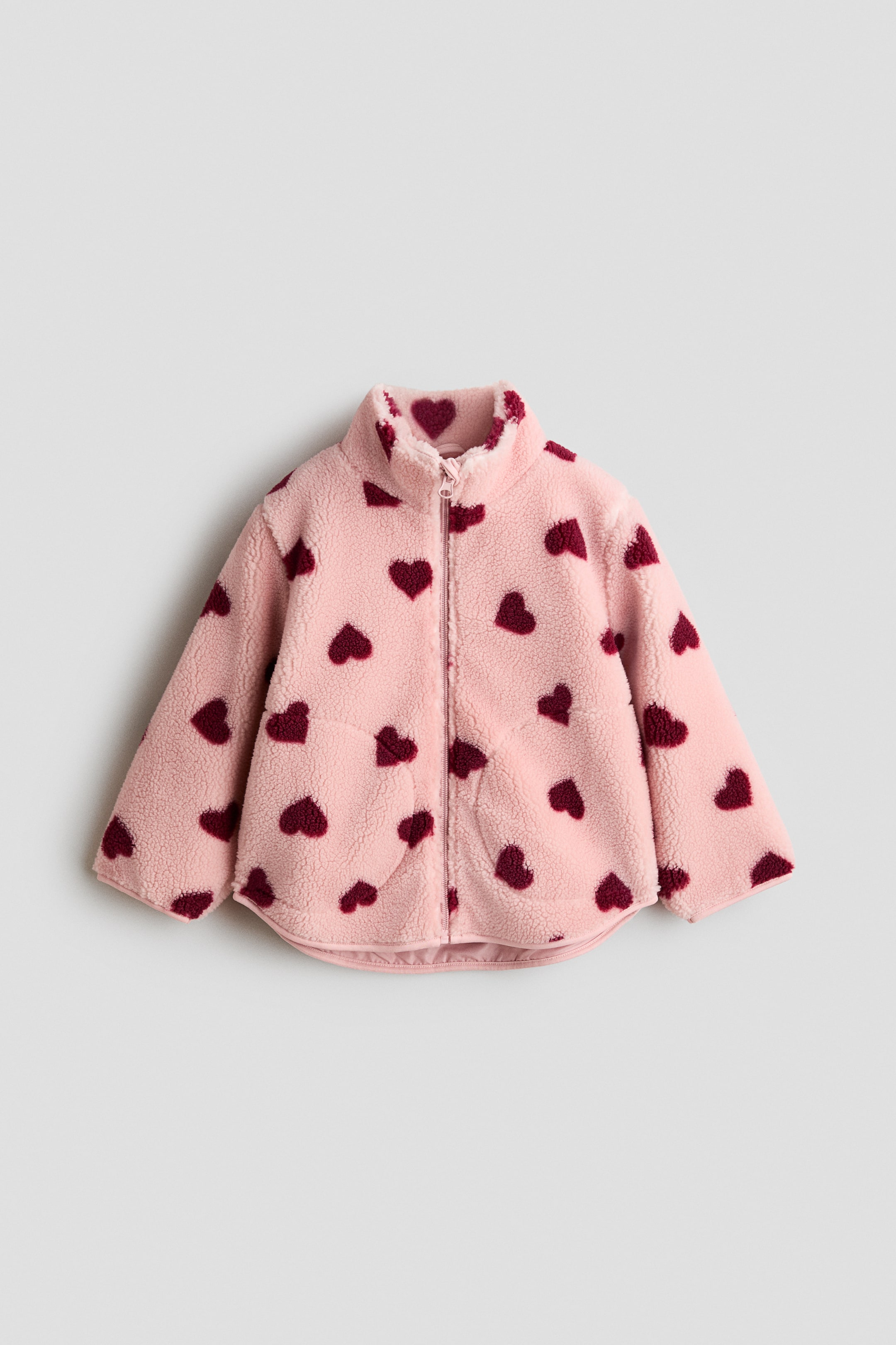 View larger image: The pink fuzzy fleece jacket boasts a full-zip front closure and a stand-up collar. It showcases an all-over dark red heart pattern, with the inside of the collar also adorned with dark red hearts, and a slightly curved hem.
