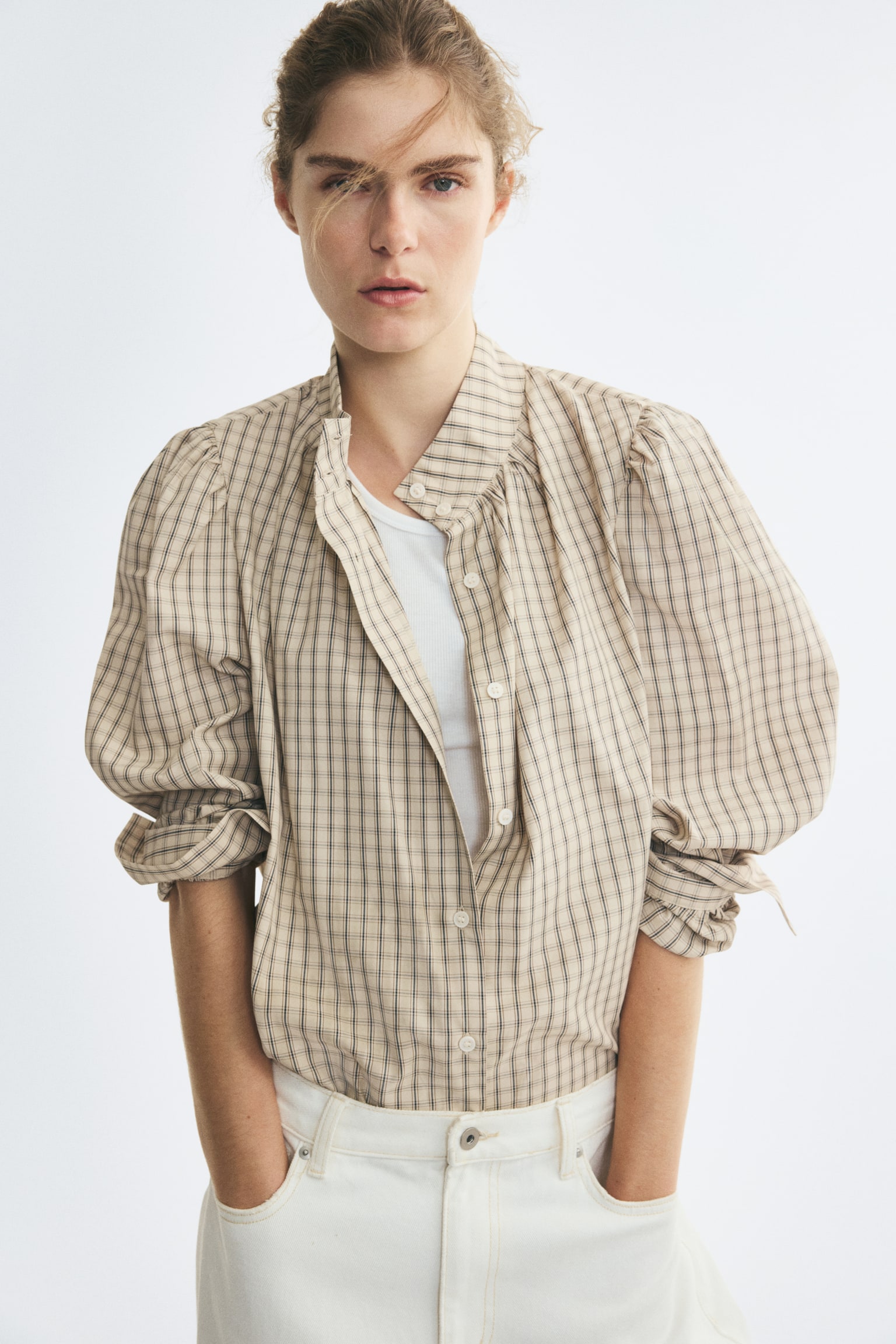 A beige plaid blouse is shown from the front, featuring a high gathered stand-up collar and a button-down front. The blouse has long puff sleeves with gathered shoulders, wide buttoned cuffs, and a curved hem. - 1