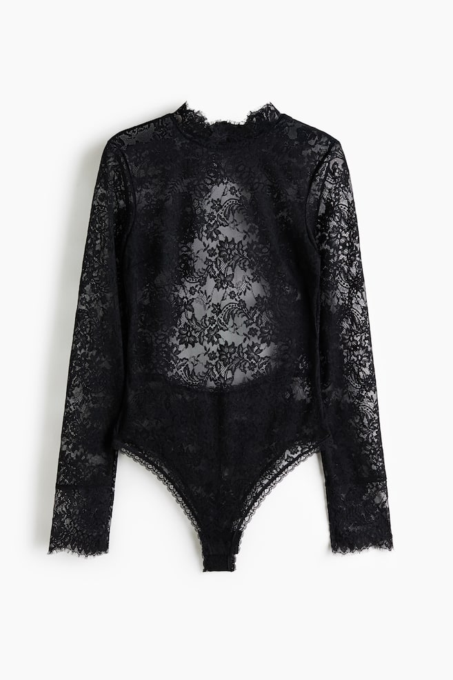 A black lace bodysuit is shown front-on, featuring sheer floral lace, long sleeves, and a high mock neck. Delicate scalloped eyelash lace trim details the collar, cuffs, and leg openings. - 1