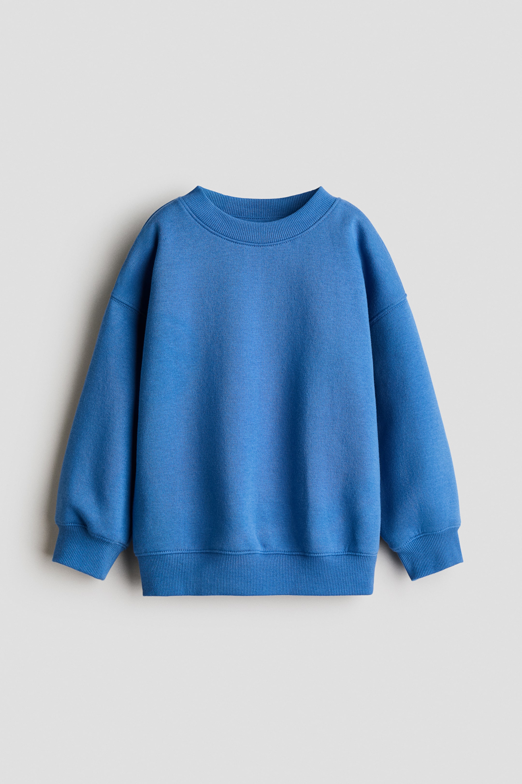 Büyük resmi görüntüle: Mavi bir sweatshirt düz bir şekilde, öne doğru yerleştirilmiş, yuvarlak, ribana detaylı bir yaka, düşük omuzlar ve ribanalı manşetler ile ribanalı etek ucu bulunan uzun kollara sahiptir.
