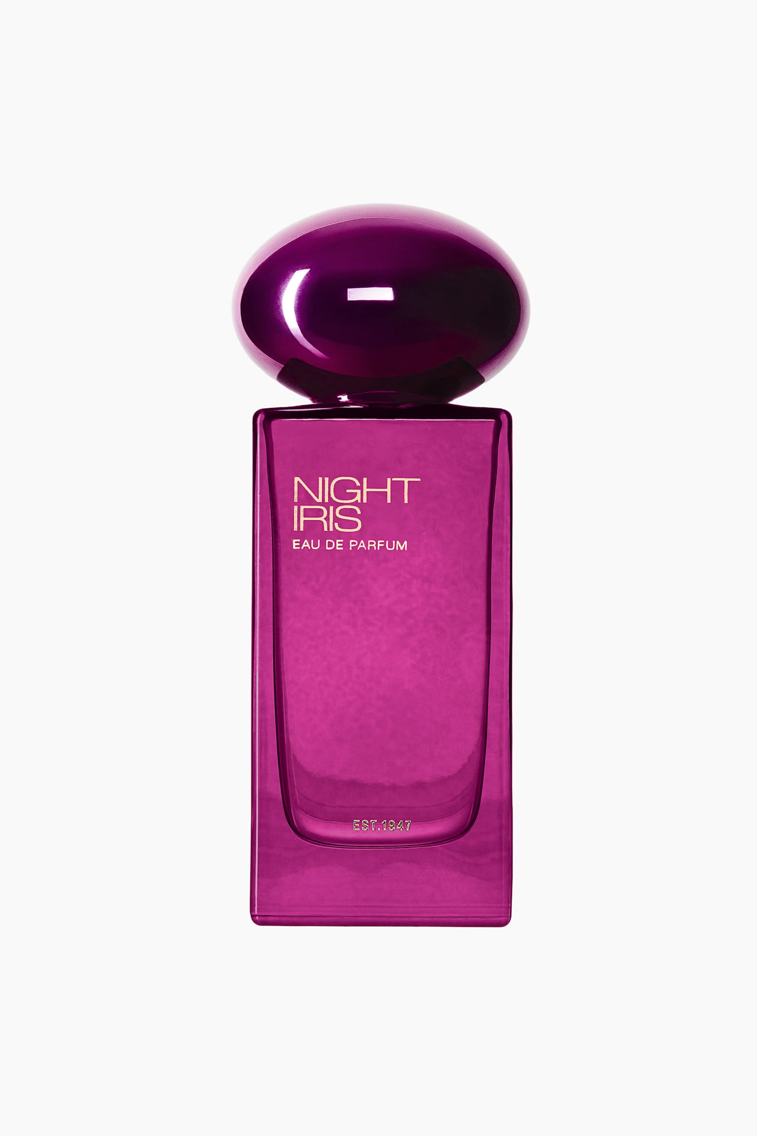 A bottle of Night Iris Eau de Parfum is shown from the front, featuring a rectangular, translucent magenta glass body topped with a glossy, dome-shaped metallic purple cap. The front of the bottle is printed with the text "NIGHT IRIS" and "EAU DE PARFUM" in gold lettering, with "EST. 1947" visible near the base.
