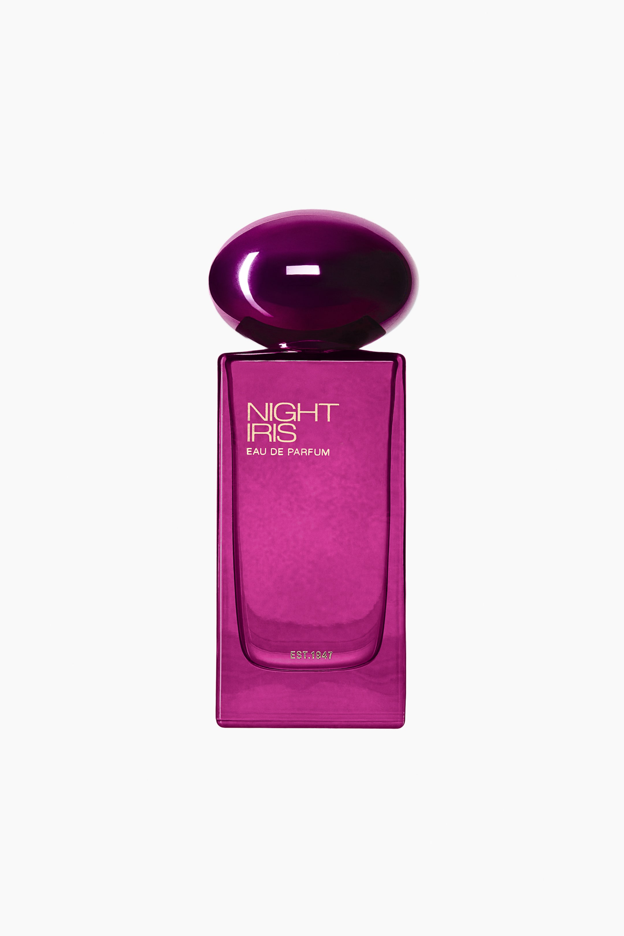 Vis større bilde: En flaske Night Iris Eau de Parfum vises forfra, med en rektangulær glasskropp i magenta og en avrundet metallisk lilla kork. Forsiden av flasken viser «NIGHT IRIS» og «EAU DE PARFUM» i gullfarget skrift, med «EST. 1947» trykt nær bunnen.