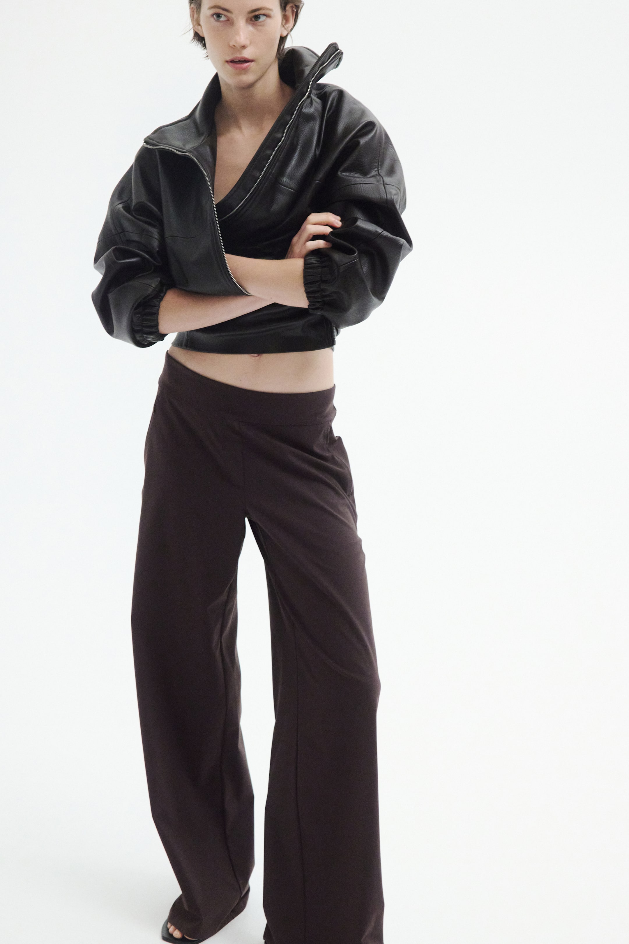 View larger image: These dark brown wide-leg pants are shown from the front, featuring a relaxed fit and falling smoothly to the floor. The pants have a flat, elasticised waistband and are styled with a cropped black jacket to highlight the clean waist design.