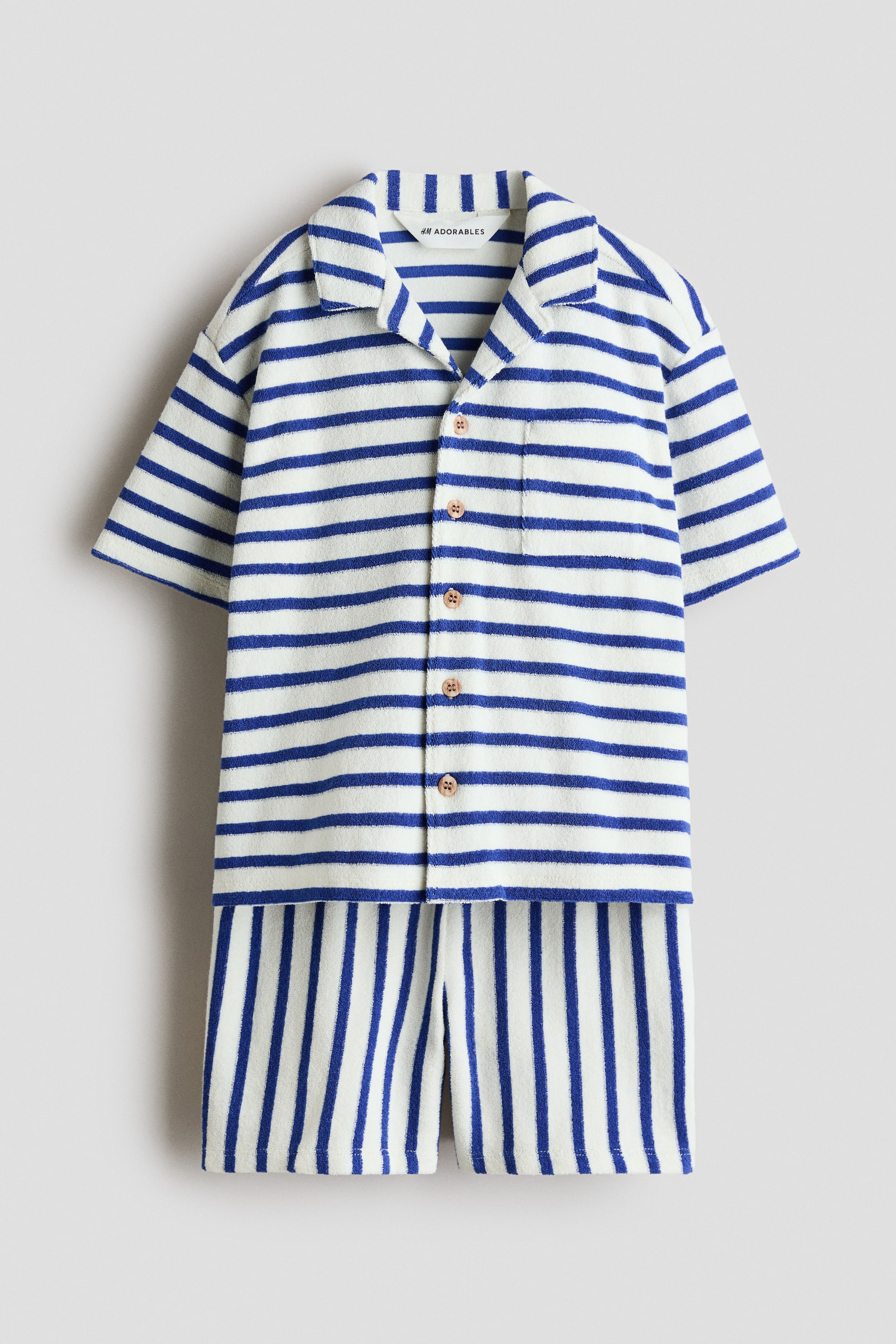 View larger image: A front-facing set features a short-sleeved shirt and shorts crafted from blue and white striped terry cloth. The shirt showcases horizontal stripes, a resort collar, dropped shoulders, light brown buttons down the front, and a patch chest pocket. The shorts display vertical stripes.