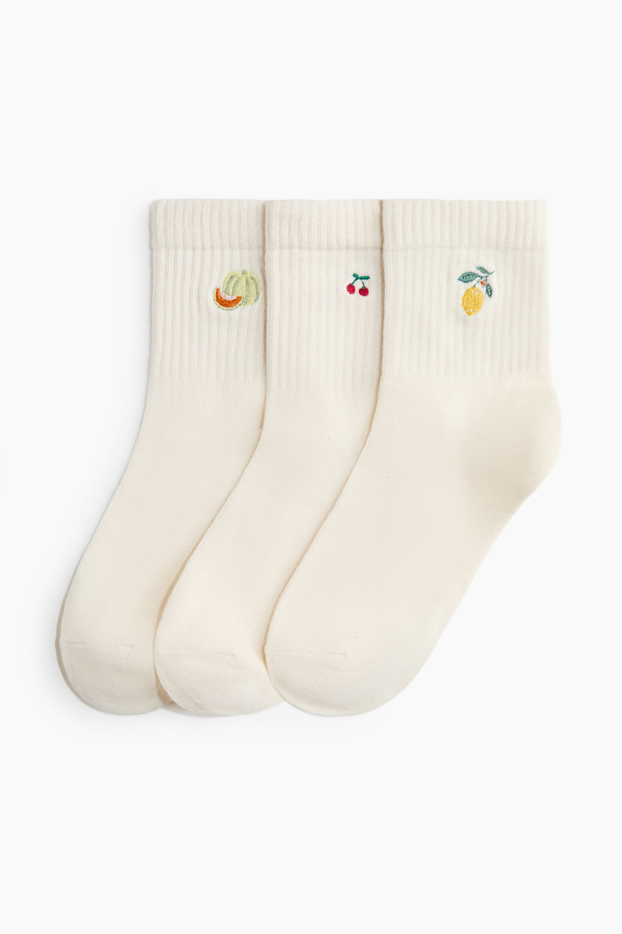 Ver imagen más grande: Calcetines en una mezcla de algodón de punto fino con cañas acanaladas y partes superiores elásticas se presentan en un conjunto de tres piezas de color crema, colocadas una al lado de la otra desde el frente. Cada calcetín está adornado con un pequeño diseño de fruta bordada en su lado exterior: una rodaja de melón, cerezas y un limón.