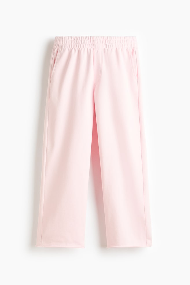 Pantalon rose à jambes larges et raccourcies posé à plat, face avant. Il présente une taille élastiquée, des poches latérales en biais et des ourlets à bord brut. - 1