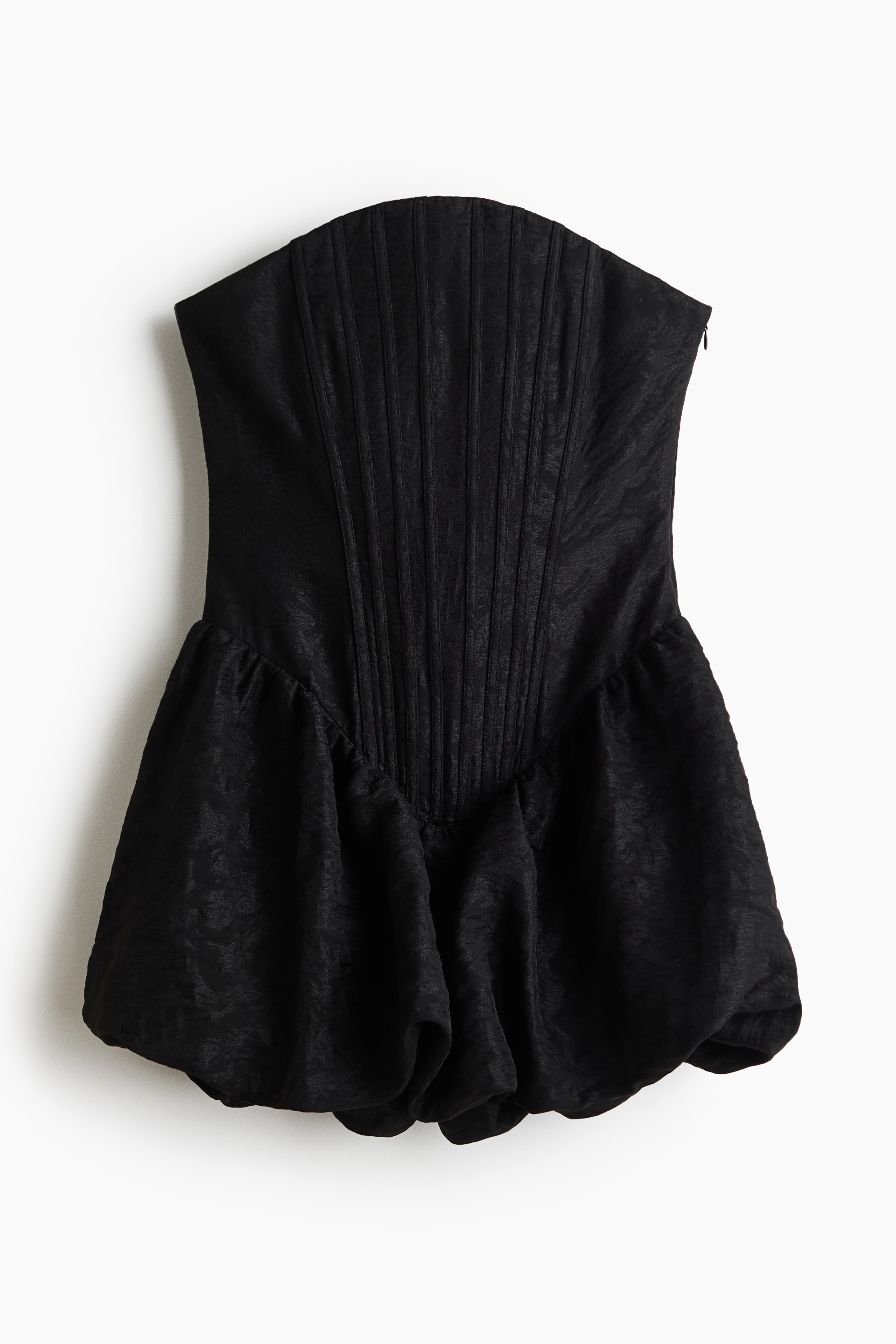 Une mini-robe bandeau noire, dotÃ©e dâun bustier corsetÃ© structurÃ© et ajustÃ© ainsi que dâune jupe boule volumineuse, est portÃ©e par le mannequin. La robe est assortie Ã  des collants noirs transparents, et le mannequin tient une petite pochette Ã  chaÃ®ne argentÃ©e.