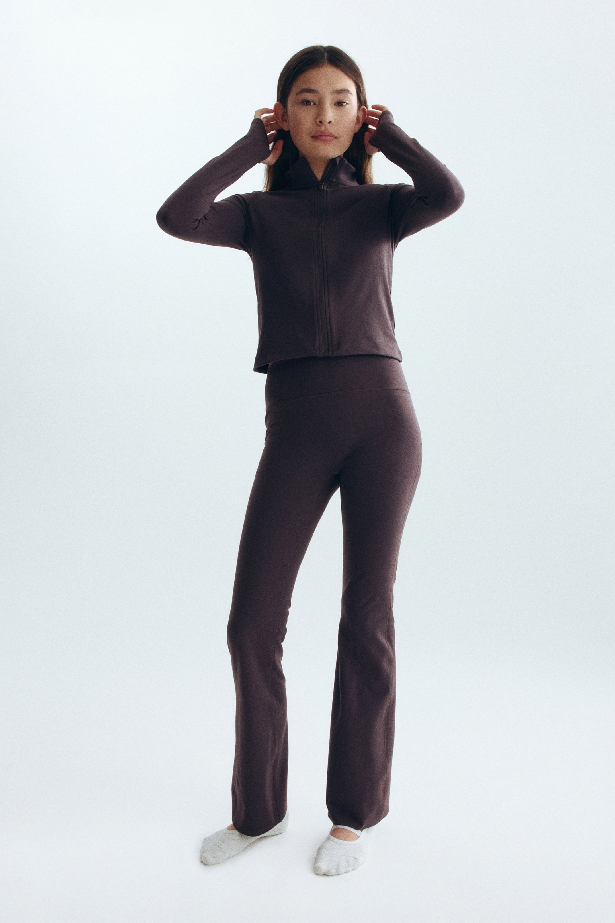 Agrandir l'image: Un ensemble sportif marron foncé est présenté, comprenant une veste courte à fermeture éclair intégrale avec un col montant et des poignets à passe-pouce, ainsi qu'un pantalon évasé taille haute assorti.