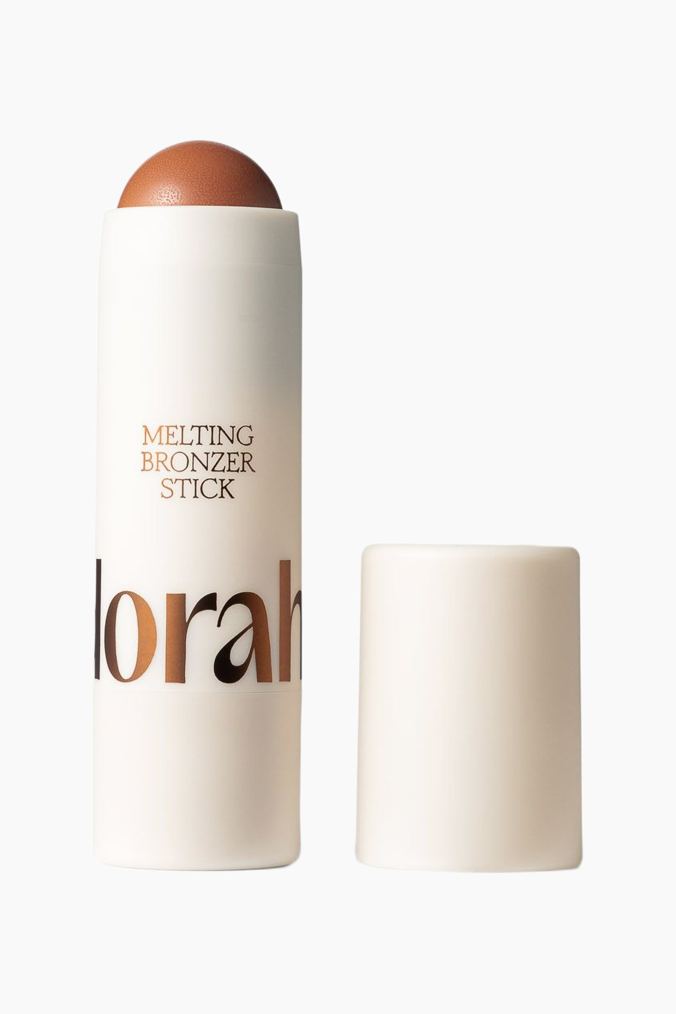 Se større billede: En lys beige cylindrisk bronzerstift præsenteres med hætten fjernet, hvilket afslører et kuplet, brun-orange bronzerprodukt, der kommer til syne fra toppen. Stiften viser "MELTING BRONZER STICK" og "lorah" i guldbogstaver, mens dens matchende lys beige cylindriske hætte står oprejst ved siden af.