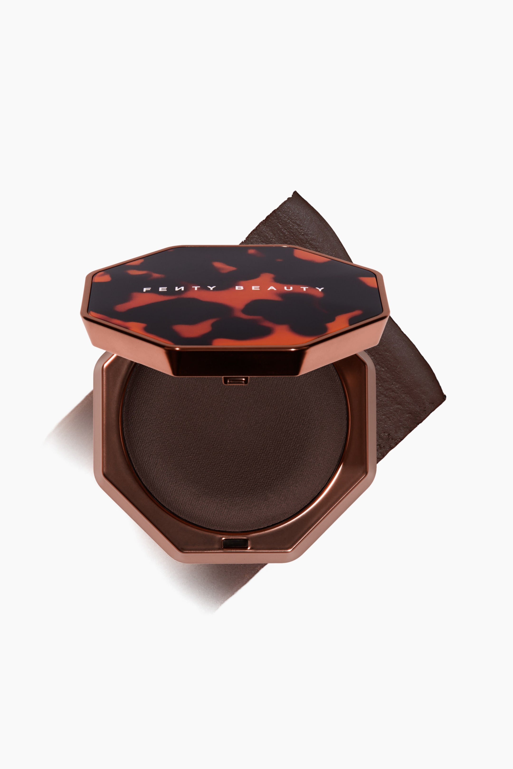 Visa större bild: En öppen, åttkantig sminkkompakt visar en mörkbrun bronzer i en metallisk koppartonad botten, med det sköldpaddsmönstrade locket delvis uppfällt för att visa Fenty Beauty-logotypen. Kompakten vilar ovanpå ett texturerat diagonalt svep av samma mörkbruna bronzer, vilket framhäver dess rika pigment och jämna finish.