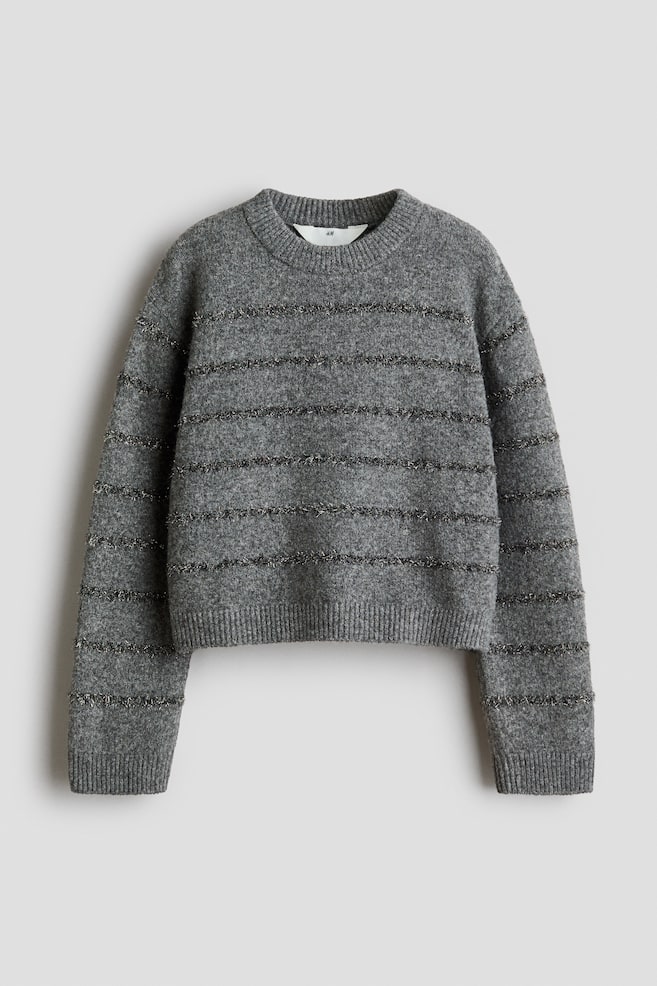 Ein grauer Strickpullover ist von vorne zu sehen und zeigt eine lockere Passform mit Ã¼berschnittenen Schultern sowie dÃ¼nnen, strukturierten, metallischen Horizontalstreifen Ã¼ber dem KÃ¶rper und den Ãrmeln. Der Pullover verfÃ¼gt Ã¼ber einen gerippten Rundhalsausschnitt, gerippte BÃ¼ndchen und einen gerippten, leicht verkÃ¼rzten Saum. - 1
