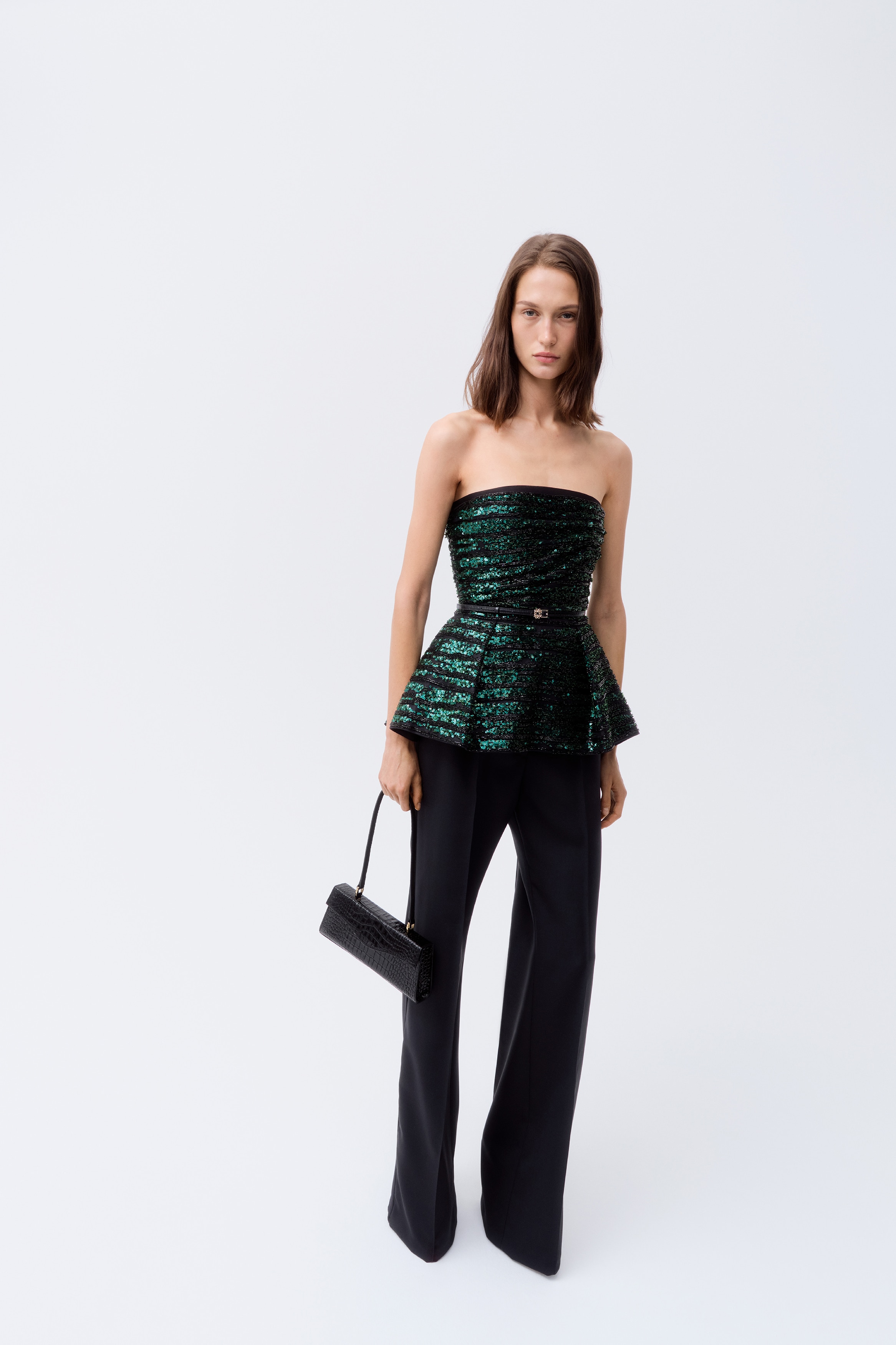An embellished peplum top is facing forward, featuring a strapless neckline and a structured bodice that flares into a pleated peplum hem. The garment showcases a pattern of alternating green sequined and black beaded horizontal stripes.