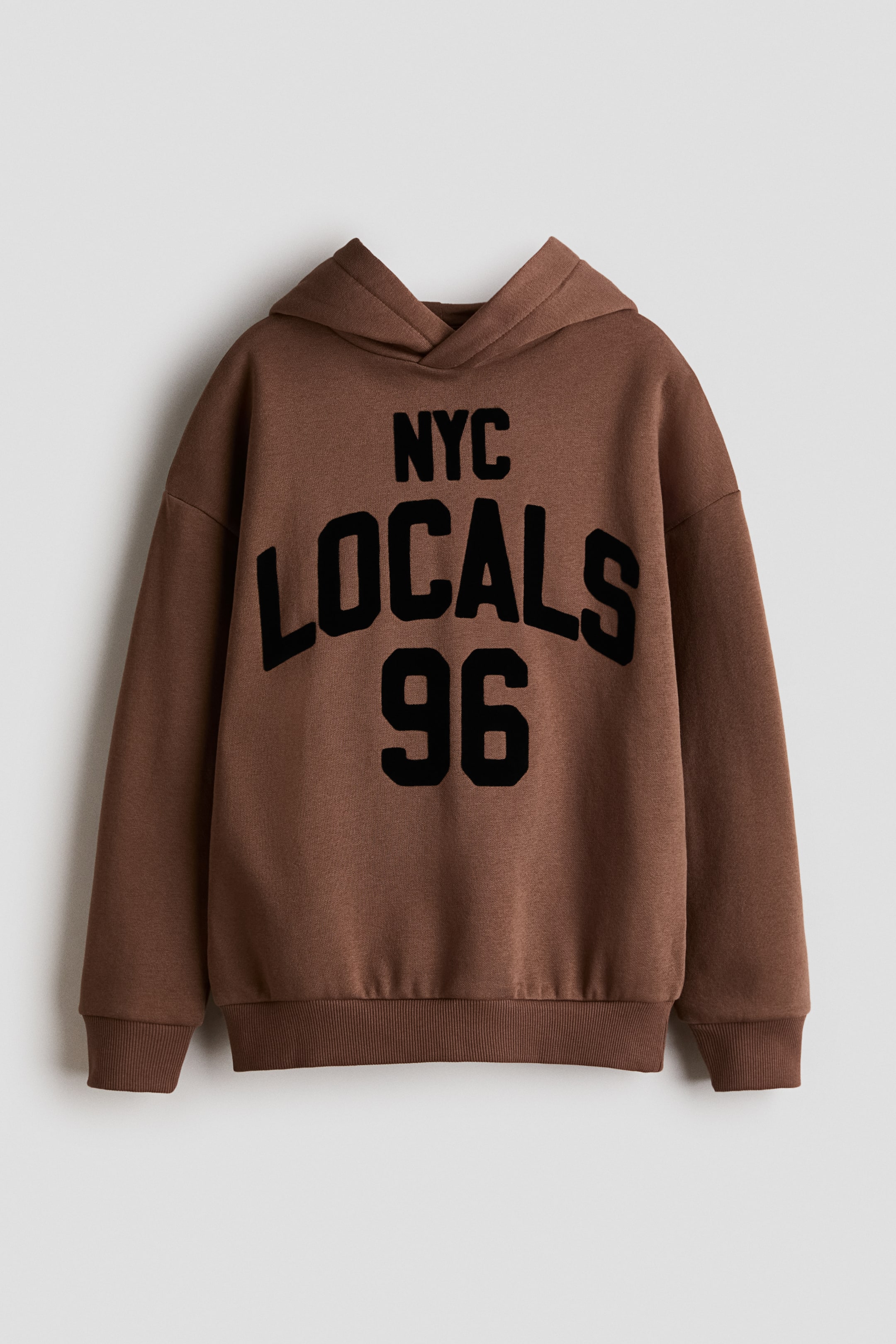 Grösseres Bild ansehen: Ein locker sitzender brauner Hoodie wird von vorne präsentiert und zeigt einen schwarzen "NYC LOCALS 96"-Print auf der Brust. Er verfügt über eine doppellagige Wickelkapuze, überschnittene Schultern, lange Ärmel sowie gerippte Bündchen und einen gerippten Saum.