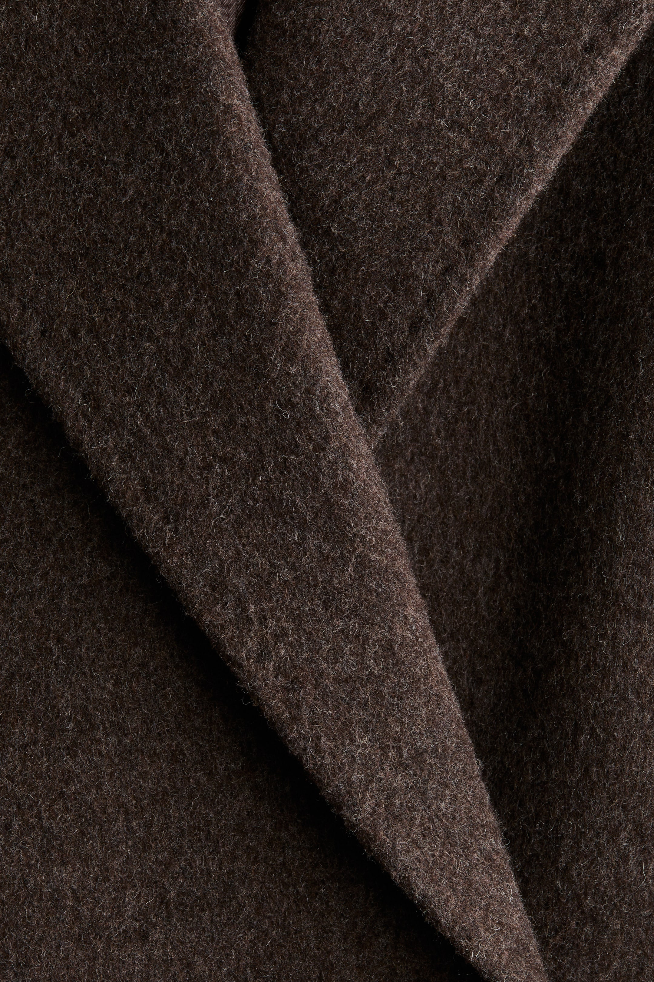 View larger image: The dark brown felted wool blend fabric of the coat is being shown up close, highlighting its soft, textured surface with a prominent diagonal fold.