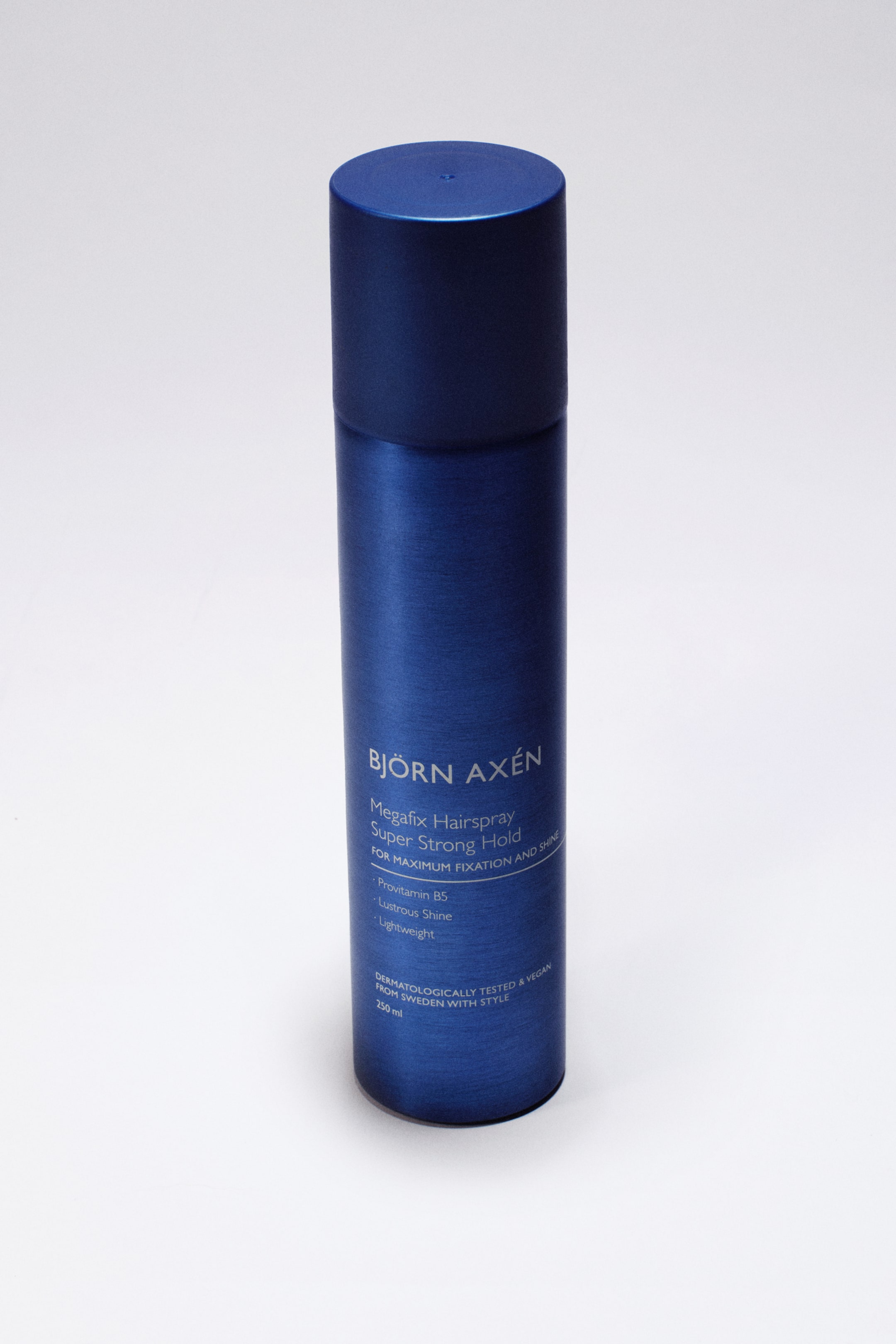 Größeres Bild ansehen: Das Megafix-Haarspray von Björn Axén steht aufrecht und zeigt eine metallisch blaue zylindrische Dose mit passender matter blauer Kappe. Die Vorderseite der Dose ist mit weißem Aufdruck versehen, der den Markennamen, Produktdetails und die wichtigsten Vorteile hervorhebt.