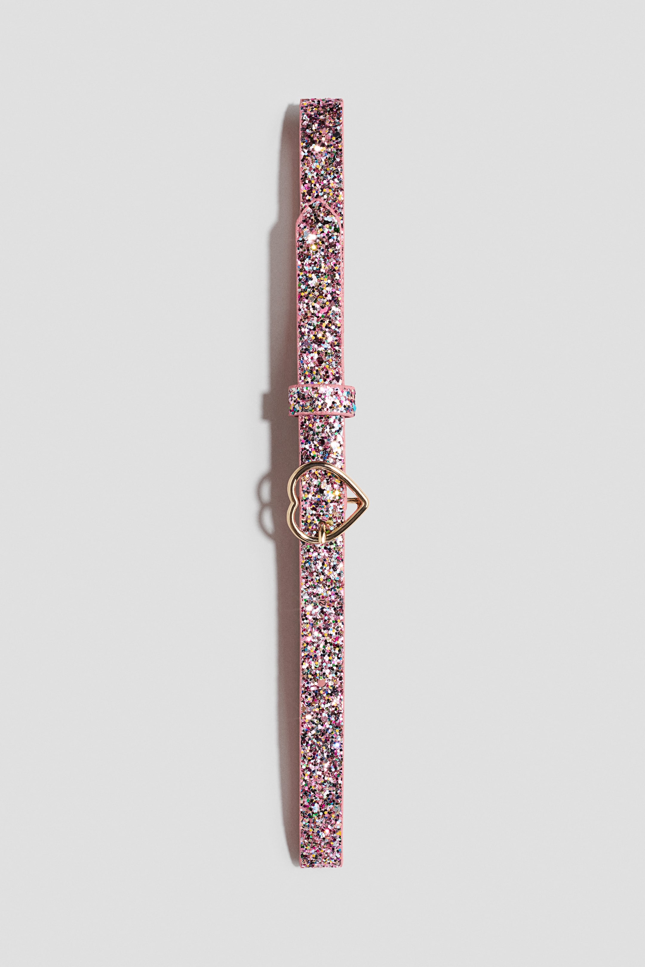 View larger image: A pink glitter belt showcases a gold-toned heart-shaped buckle. The belt also features a matching glitter strap keeper, and its strap is adorned with multi-coloured glitter.