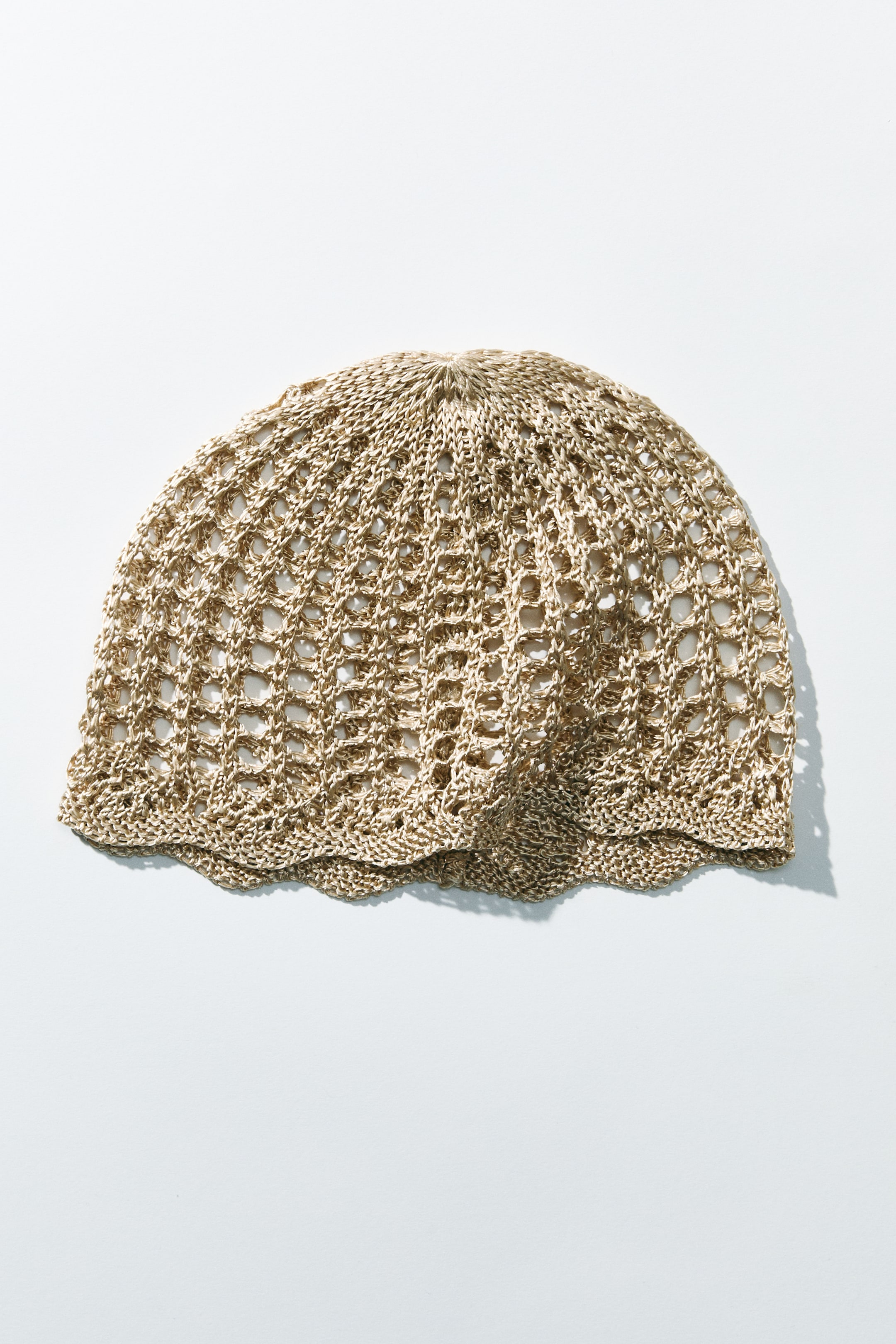 Visualizza immagine più grande: Un cappello è disteso piatto, mettendo in mostra la sua maglia viscosa scintillante con effetto crochet aperto. Presenta un motivo traforato distintivo con un bordo smerlato lungo il suo perimetro.