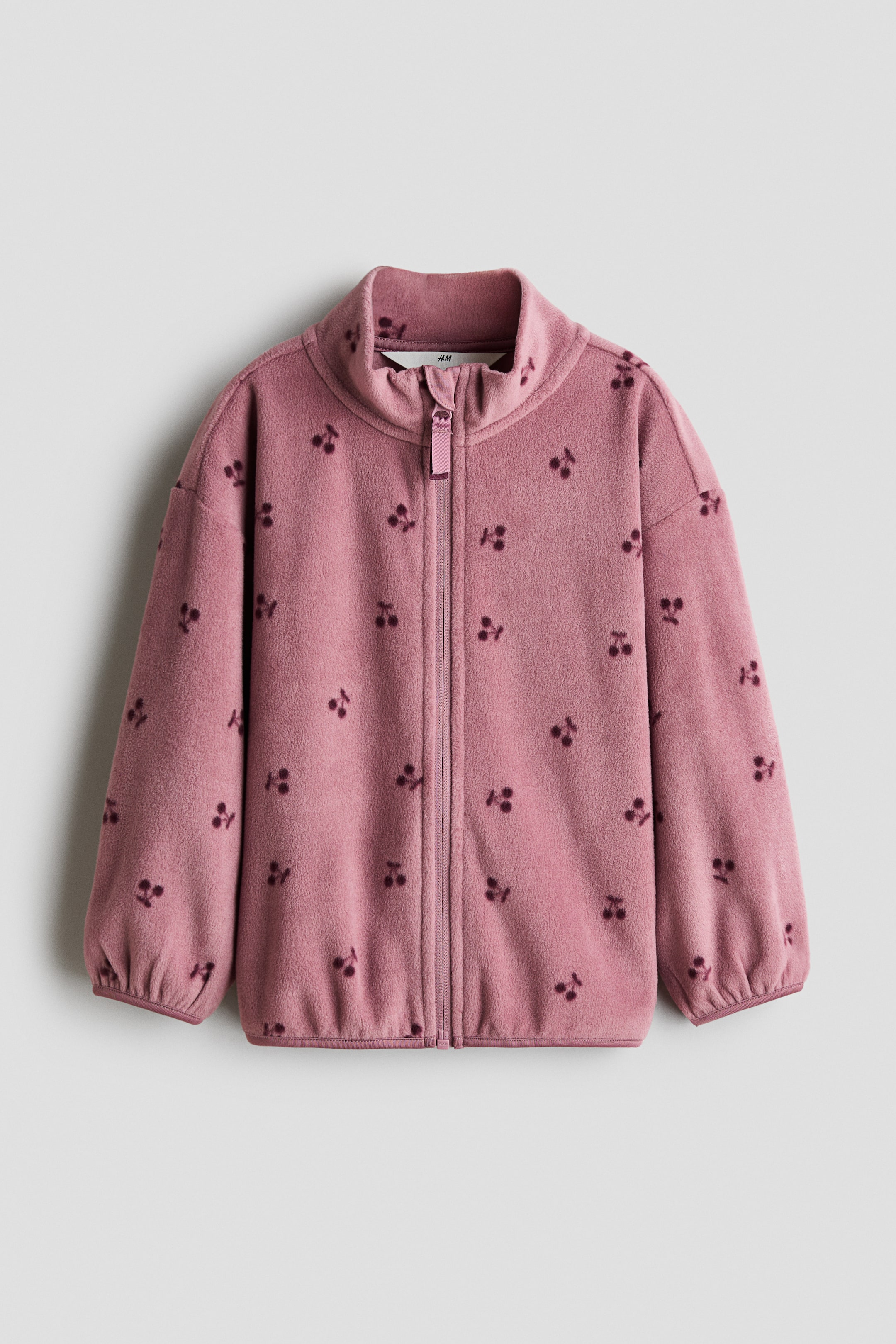 Größeres Bild anzeigen: Eine Jacke aus Fleece in Altrosa zeigt die Vorderseite und ist mit Kirschmotiven gemustert. Sie verfügt über einen Stehkragen, einen Frontreißverschluss mit Kinnschutz gegen Reibung, überschnittene Schultern sowie Paspeln an den Ärmelabschlüssen und am Saum.