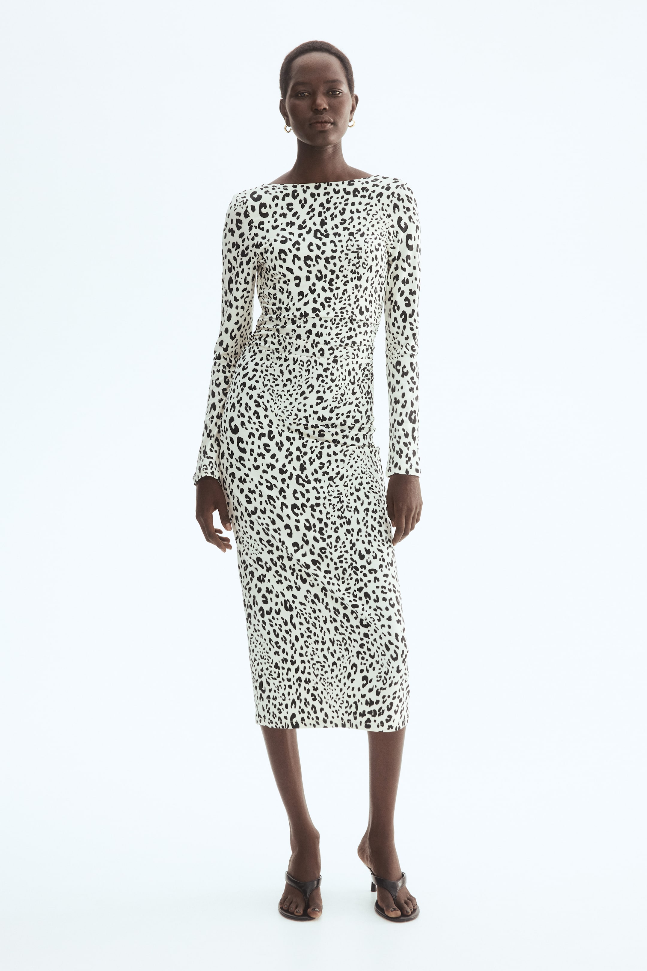 Ingrandisci l'immagine: Un abito midi a stampa leopardata bianca e nera viene presentato, caratterizzato da maniche lunghe, scollo a barca e una silhouette aderente con arricciature raccolte sul lato sinistro.