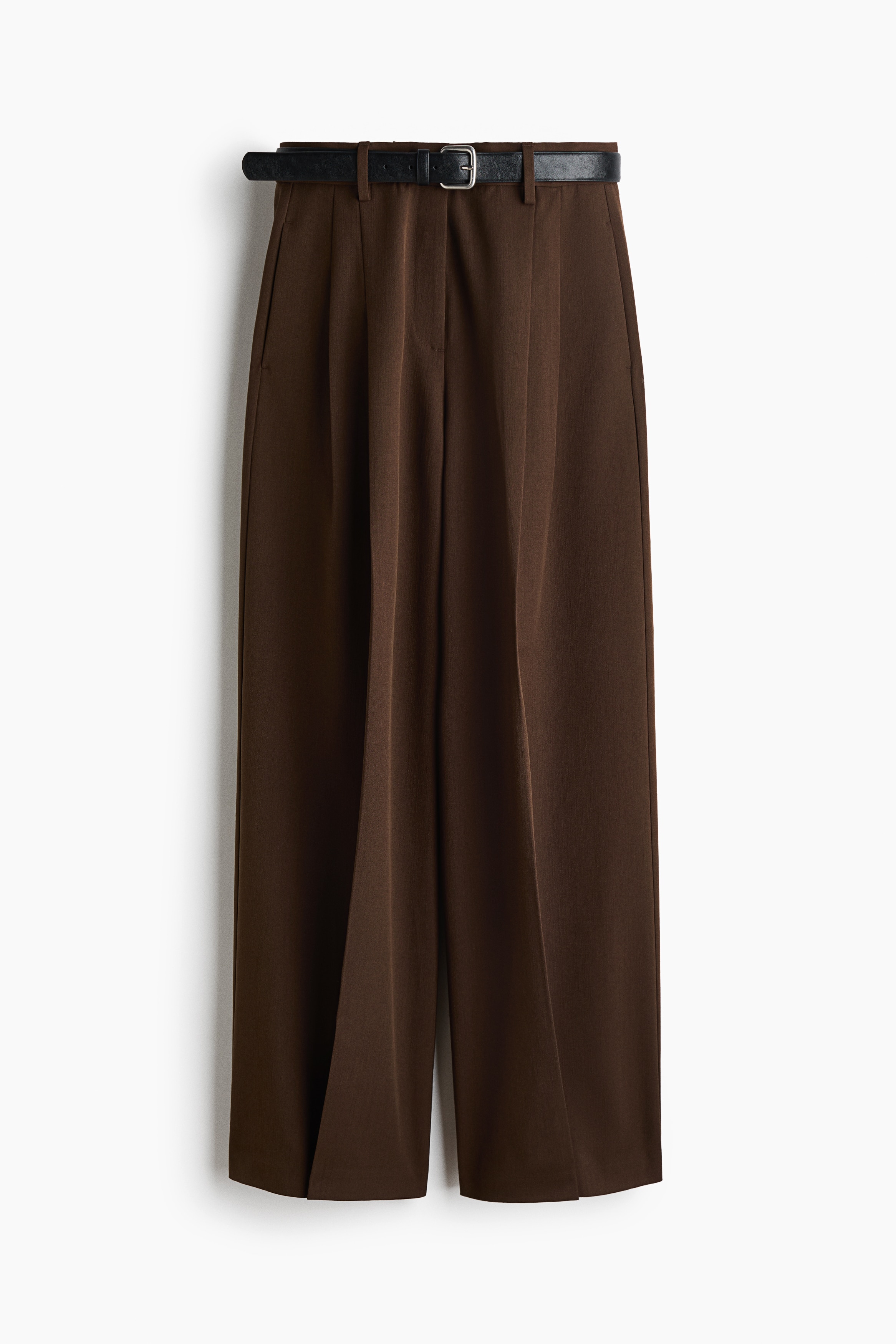 La modelo lleva pantalones color cafÃ© de corte holgado en tejido plano, con piernas amplias, pinzas al frente, marcado de raya y un cinturÃ³n negro. Los pantalones se combinan con una camiseta blanca parcialmente metida por dentro y un blazer oscuro oversize.