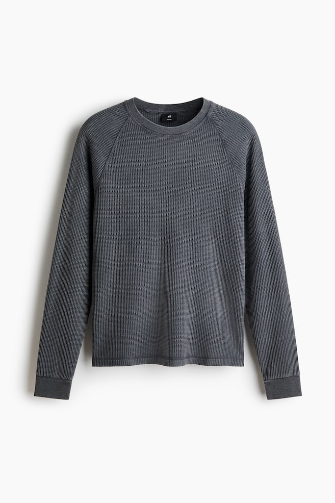 Ein dunkelgraues, langärmeliges Waffelstrick-Shirt mit Rundhalsausschnitt, Raglanärmeln und gerippten Bündchen. Das Shirt ist frontal ausgerichtet und zeigt auch einen geraden Saum. - 1