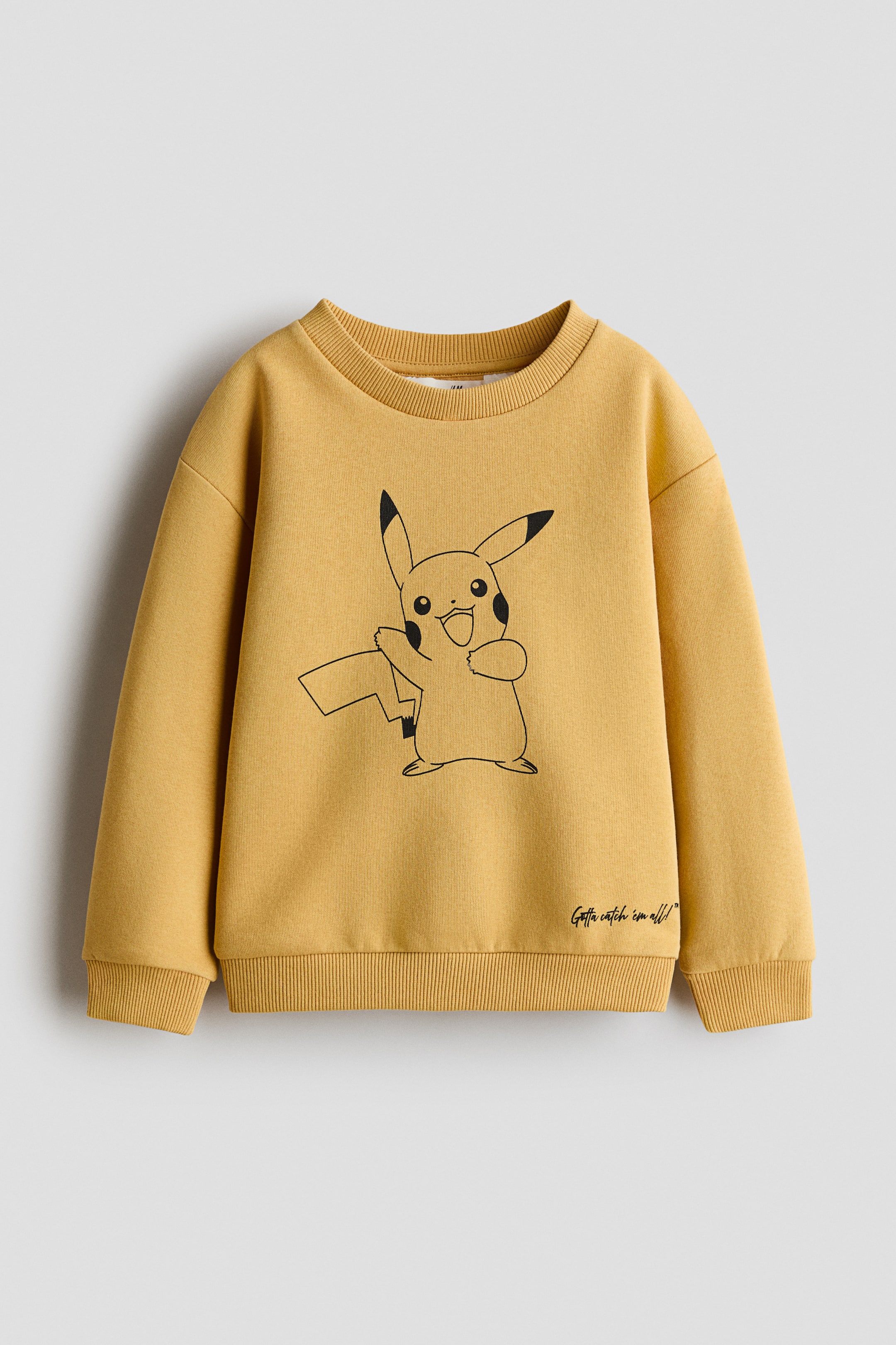 Visualizza l'immagine ingrandita: Una felpa gialla dal taglio ampio è mostrata frontalmente e presenta sul petto una stampa a contorno nero di Pikachu. La felpa è caratterizzata da un girocollo rifinito a costine, spalle scese, maniche lunghe e polsini e orlo a costine, con la scritta corsiva «Gotta catch 'em all!» stampata vicino all'angolo inferiore destro.