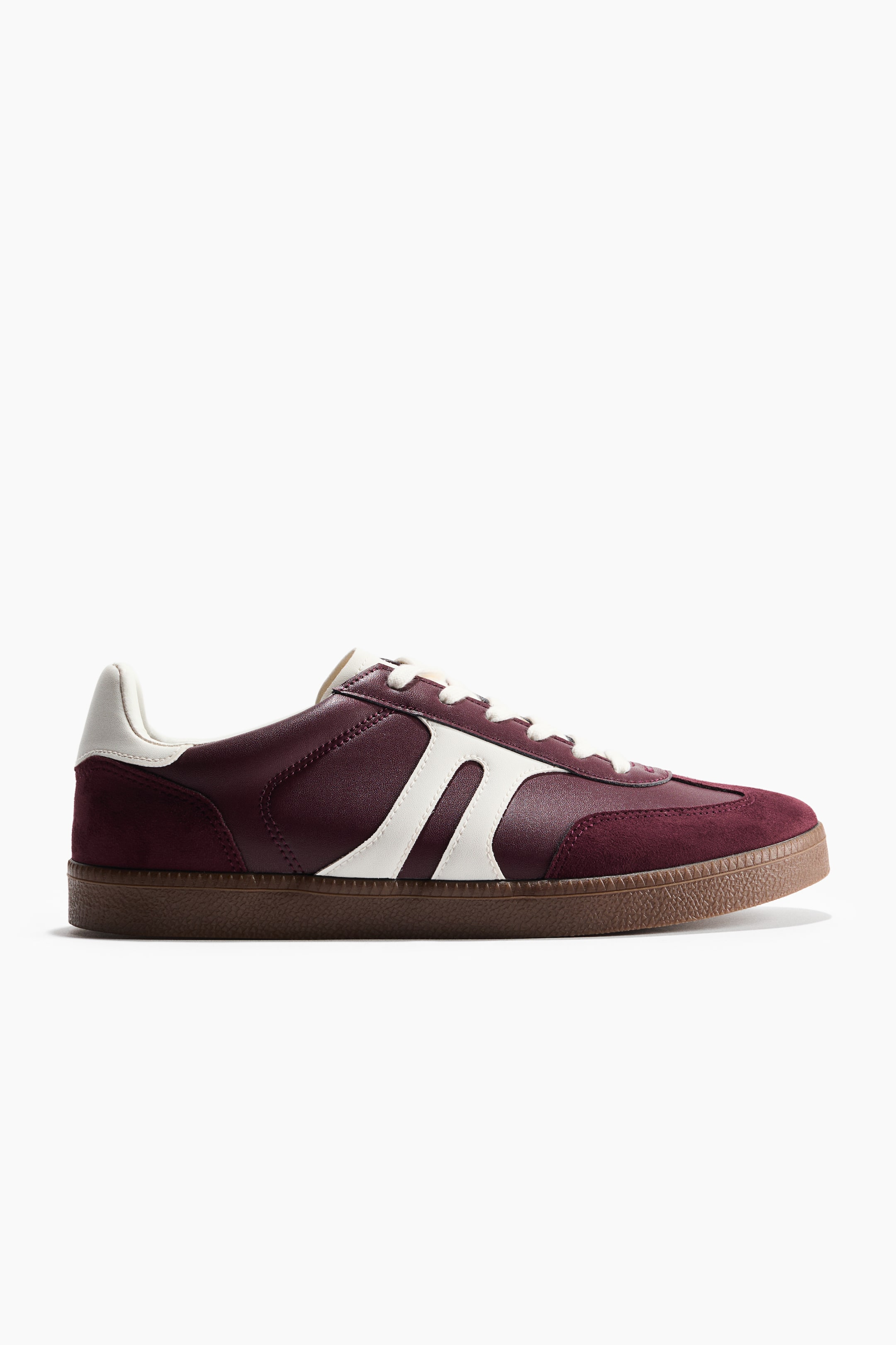 Agrandir l'image: Une sneaker basse présente une tige en cuir bordeaux avec des empiècements en daim sur la pointe et le talon. Elle est dotée de deux panneaux latéraux incurvés blancs, de lacets blancs, d'un empiècement de talon blanc, et d'une semelle en caoutchouc marron texturée.
