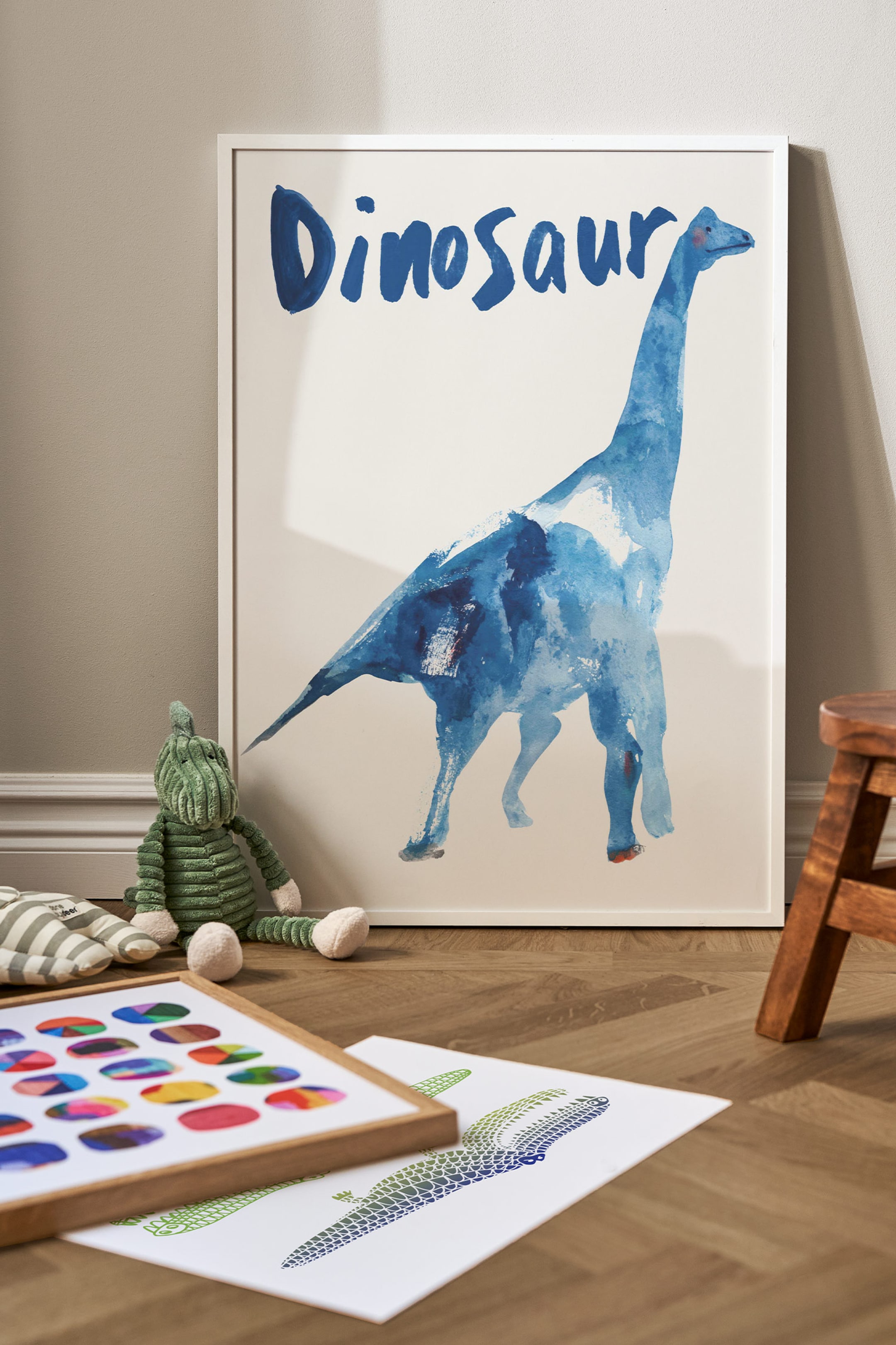 Grotere afbeelding bekijken: Een ingelijste poster toont een blauwe aquarelillustratie van een langnekdinosaurus op een effen witte achtergrond. Het woord "Dinosaur" staat bovenaan in een gestileerd, blauw handgeschilderd lettertype, en de print is omlijst met een dun wit frame.