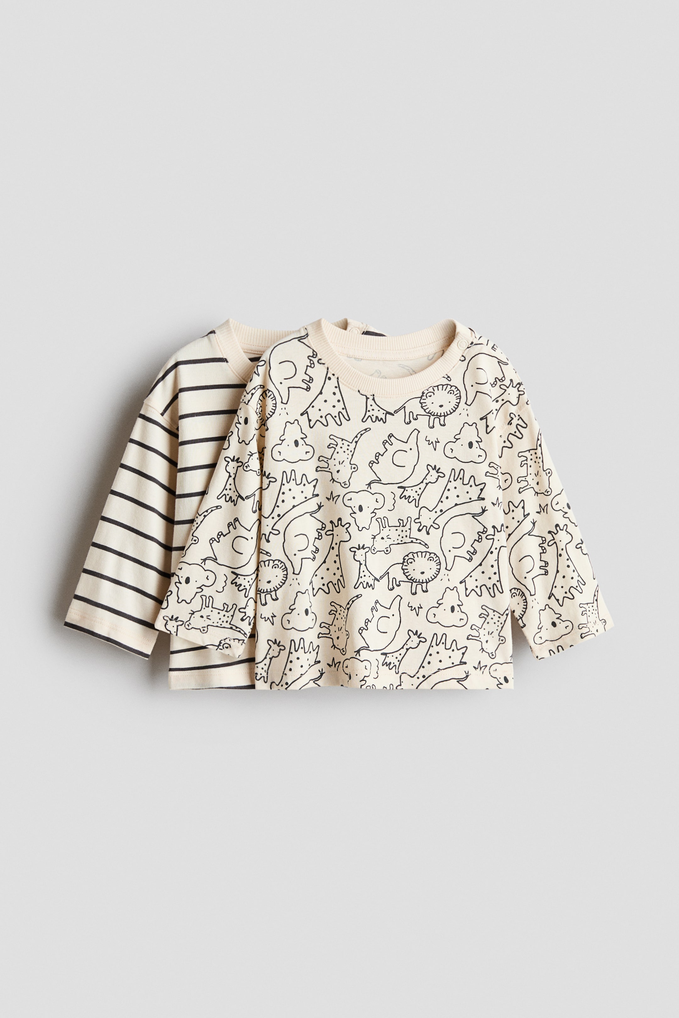 View larger image: Two long-sleeved tops are displayed, both showcasing their fronts. The front top is cream with an all-over black outline print of various cartoon animals, featuring a ribbed crew neck and shoulder snaps. The top behind is partially visible, revealing a cream fabric with black horizontal stripes and a ribbed crew neck.