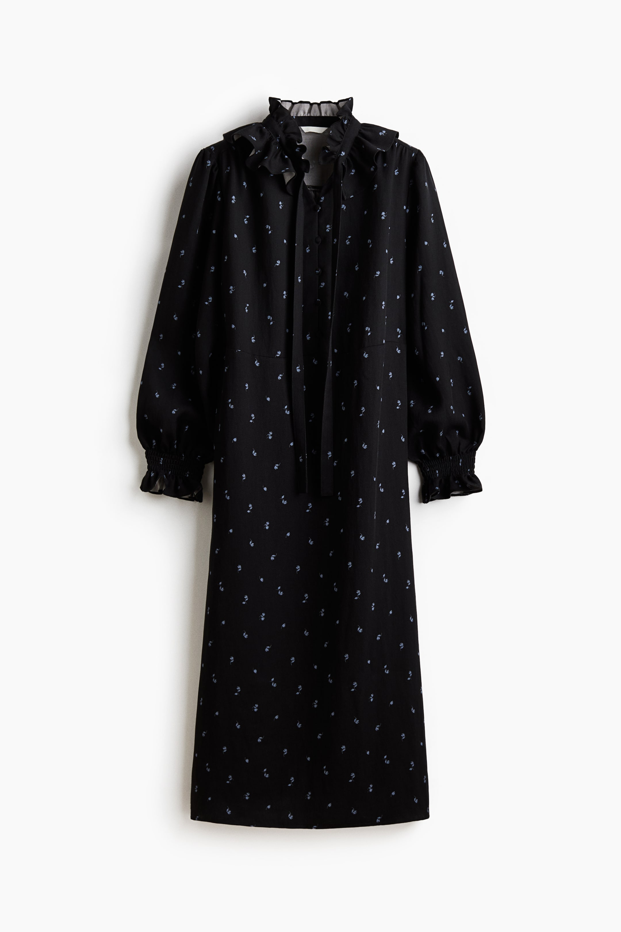 Xem ảnh lớn hơn: Một chiếc váy đen, được trưng bày MẶT TRƯỚC, có họa tiết hoa xanh lam rải rác. Nó được thiết kế với cổ cao có bèo và buộc dây, cùng tay áo dài phồng tập trung vào cổ tay có dạng smocked. Chiếc váy có dáng thẳng, dài tới đầu gối.