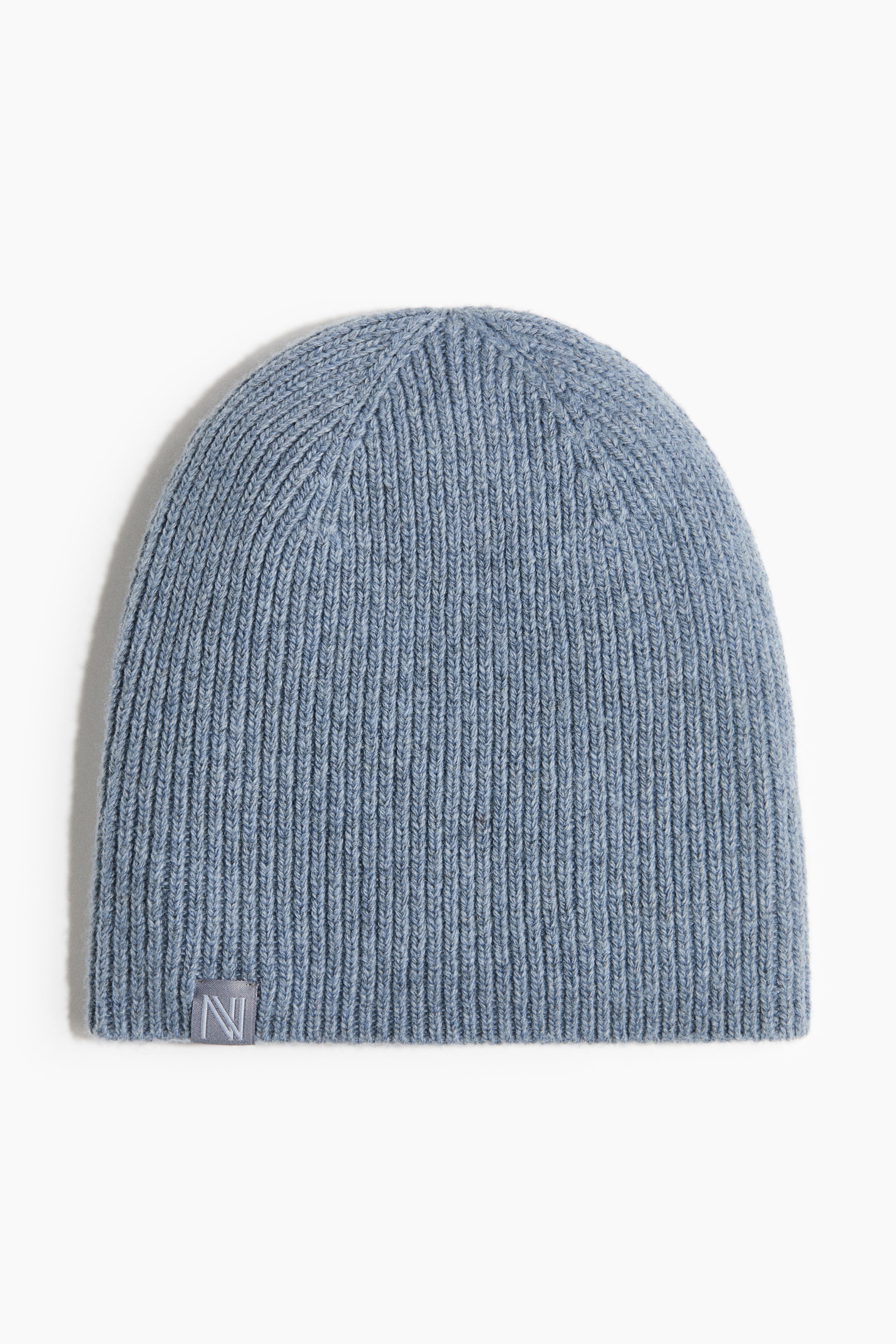 View larger image: A light blue ribbed knit beanie is showcased, facing front. A small, rectangular grey tag with a darker grey letter "N" is affixed to the front's lower left edge.