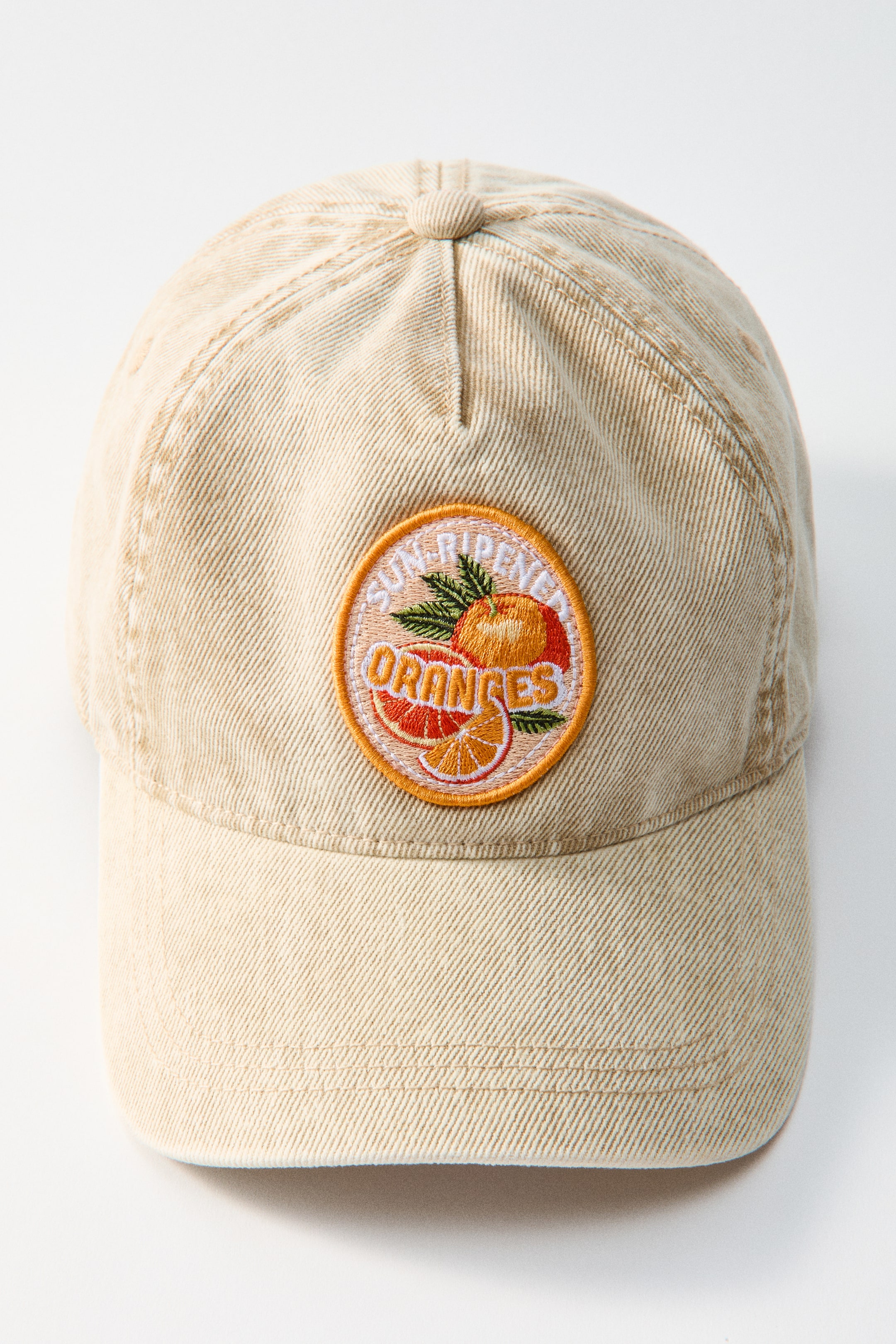 View larger image: A beige washed cotton twill baseball cap is facing forward, showcasing a circular embroidered patch on its front. The patch features a whole orange, two orange slices, and green leaves, with the words 'SUN-RIPENED ORANGES' embroidered in white against a light orange background and an orange border.