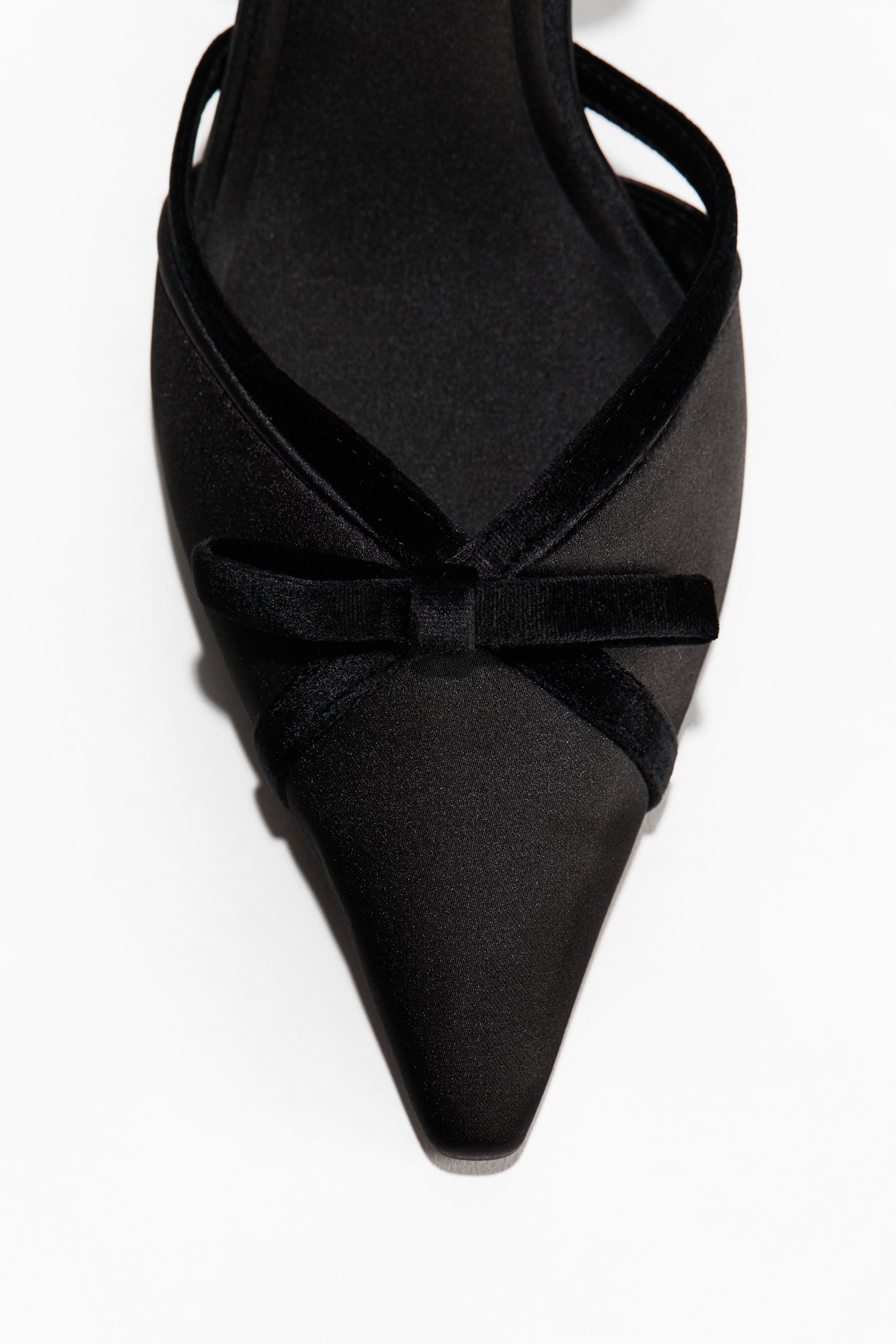 Black satin slingback shoes featuring pointed toes and velvet bow details are being worn by the model. The slingbacks are styled over slouchy, grey ribbed socks embellished with small rhinestones.