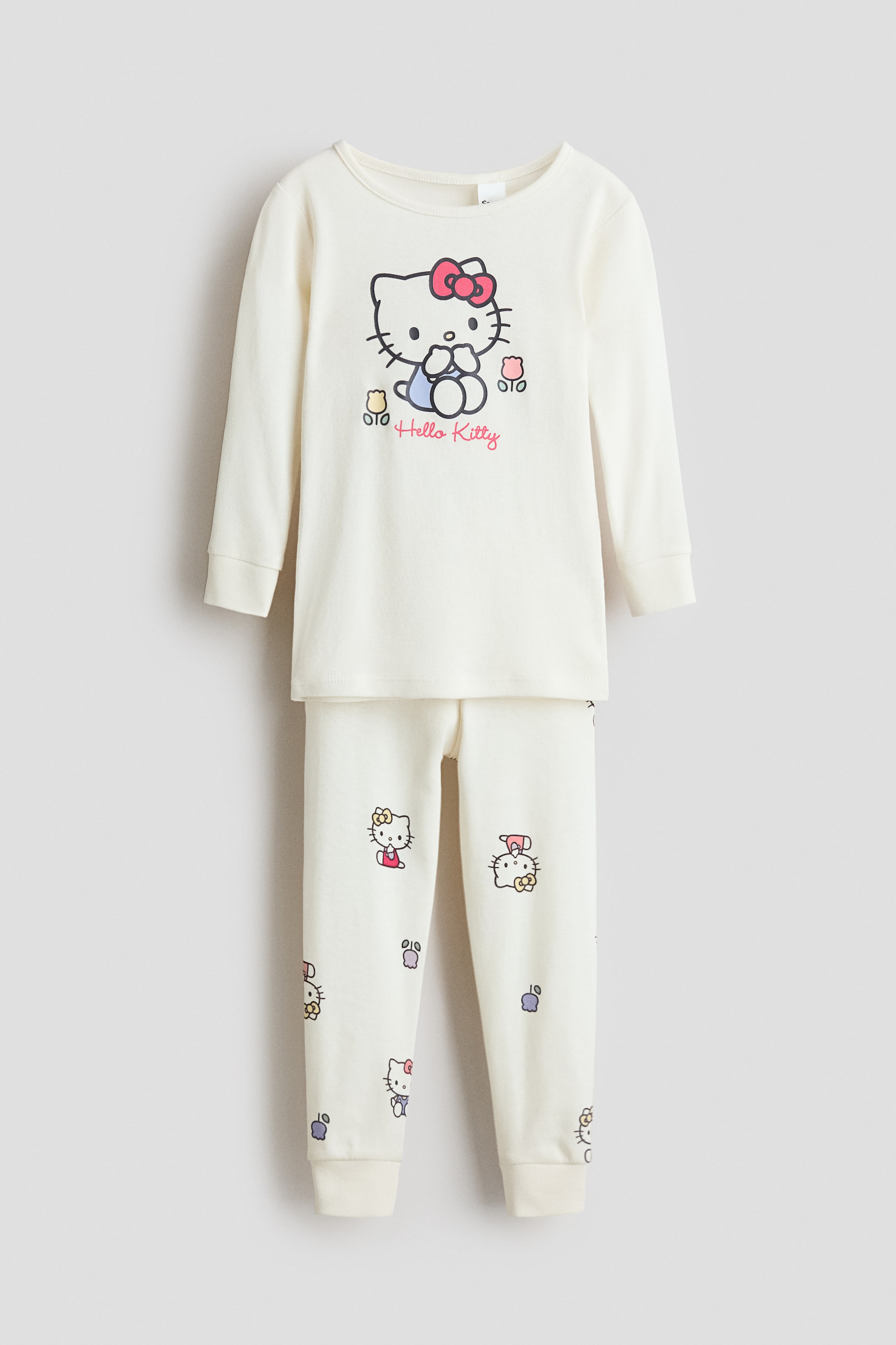 View larger image: A cream-colored two-piece pajama set is facing FRONT. The long-sleeved top features a round neckline, ribbed cuffs, and a large Hello Kitty graphic on its front. The matching full-length bottoms display smaller, scattered Hello Kitty designs and ribbed cuffs at the ankles.