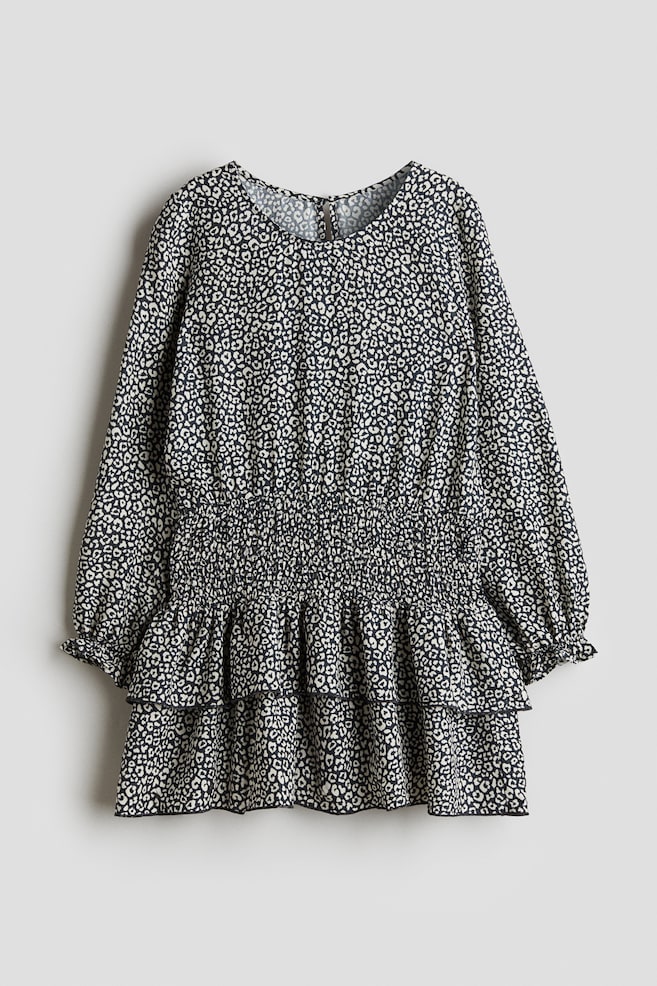 A dress is featuring a black and white abstract animal print. Its front is displaying a round neckline, long sleeves with gathered cuffs, a wide shirred elasticated waistband, and a two-tiered ruffled hemline. - 1
