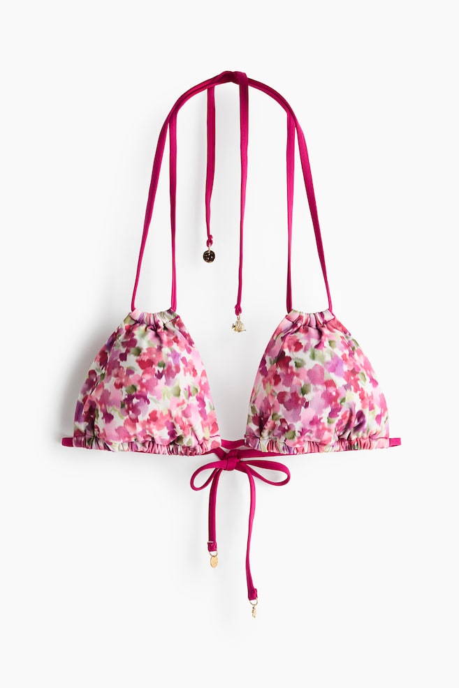 Il top bikini presenta uno stile triangolare frontale con coppe arricciate. È caratterizzato da una stampa floreale in tonalità di rosa, viola e verde, mentre i lacci magenta si estendono dalla parte superiore di ciascuna coppa e dal fondo, con i lacci inferiori che si legano al centro davanti, e piccoli ciondoli dorati adornano alcune estremità dei lacci. - 1