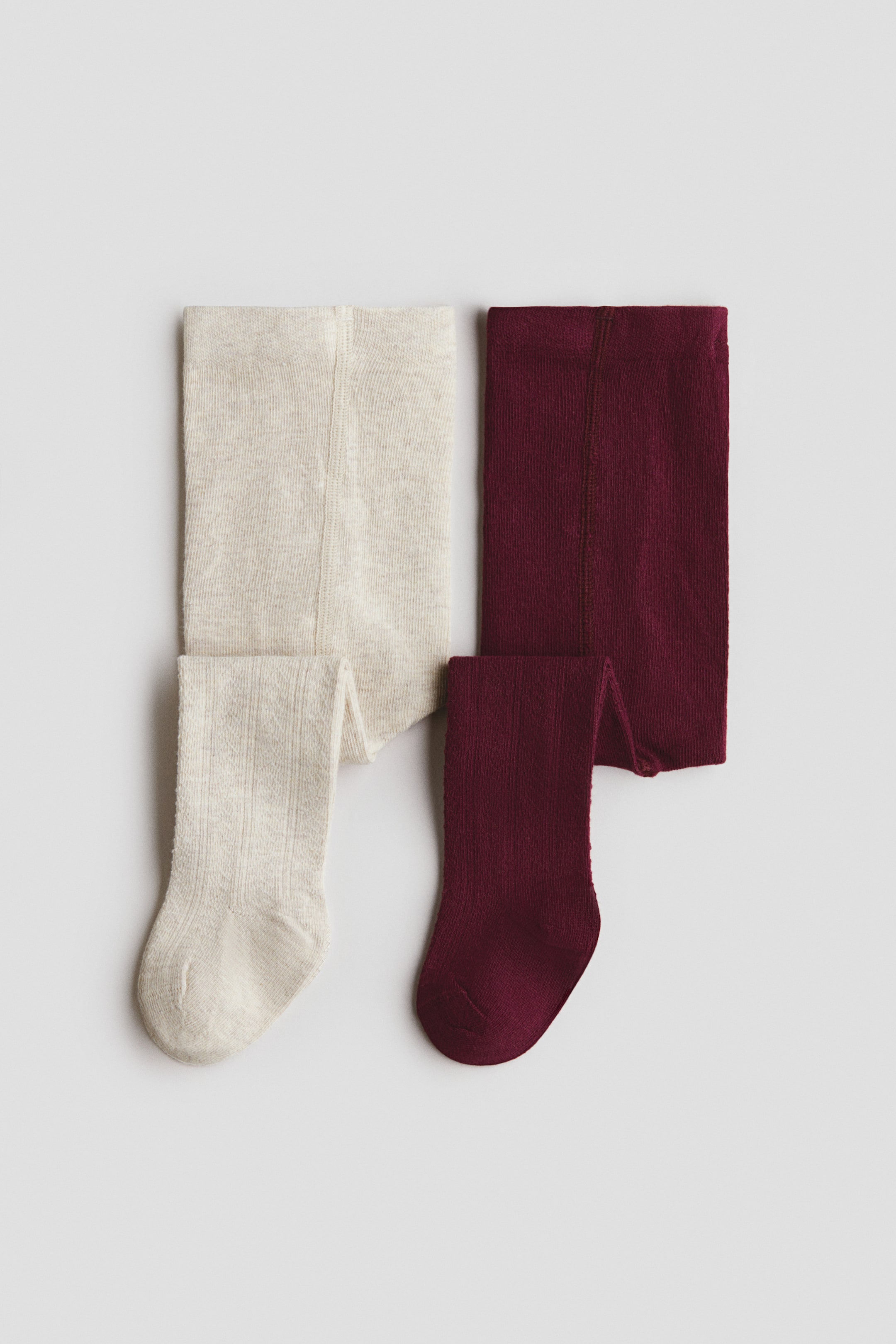 View larger image: Two pairs of ribbed knit tights, one in heathered cream and the other in deep burgundy, are laid flat side by side, with one leg of each pair folded forward to show the foot shape.