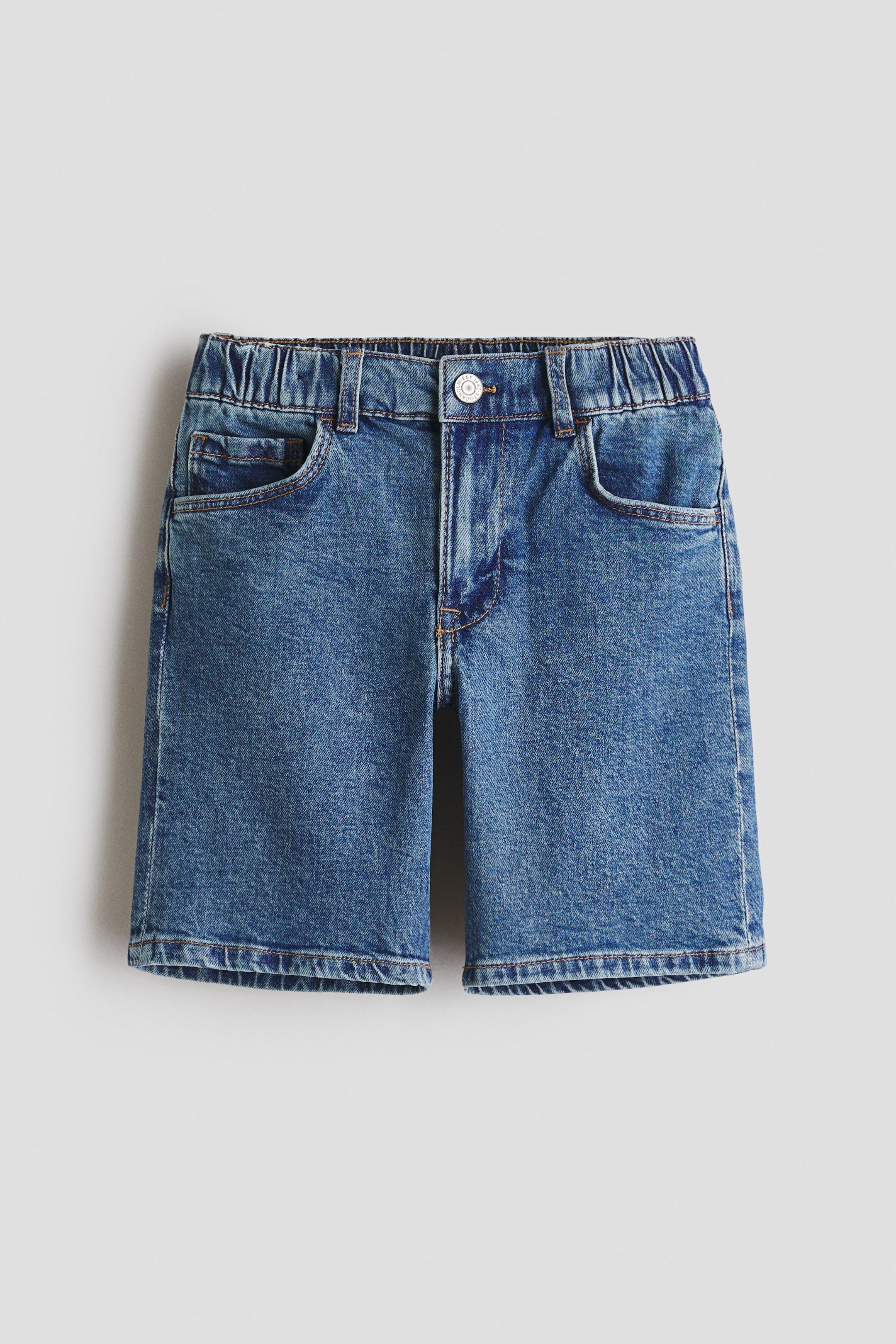 View larger image: Denim shorts feature a faded medium blue wash, an elasticated waistband with belt loops, a front button and zipper closure, two front pockets, and a straight hem with visible contrasting stitching, all shown from the front.