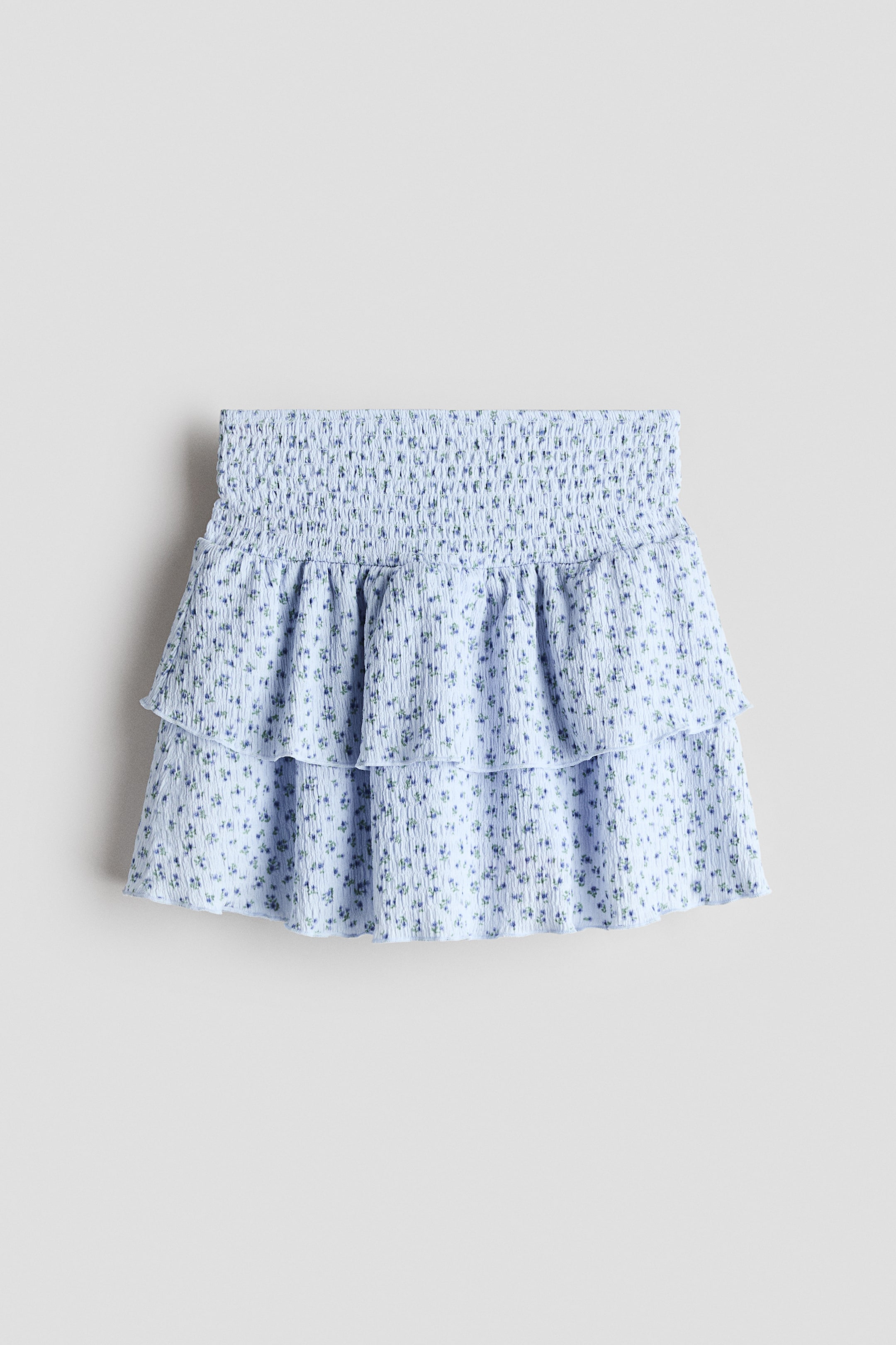 Ver imagen más grande: La falda escalonada de jersey arrugado y estampado muestra su vista frontal. Presenta una cinturilla fruncida, dos volantes escalonados y bordes sobrehilados, en color azul claro con un pequeño estampado floral.