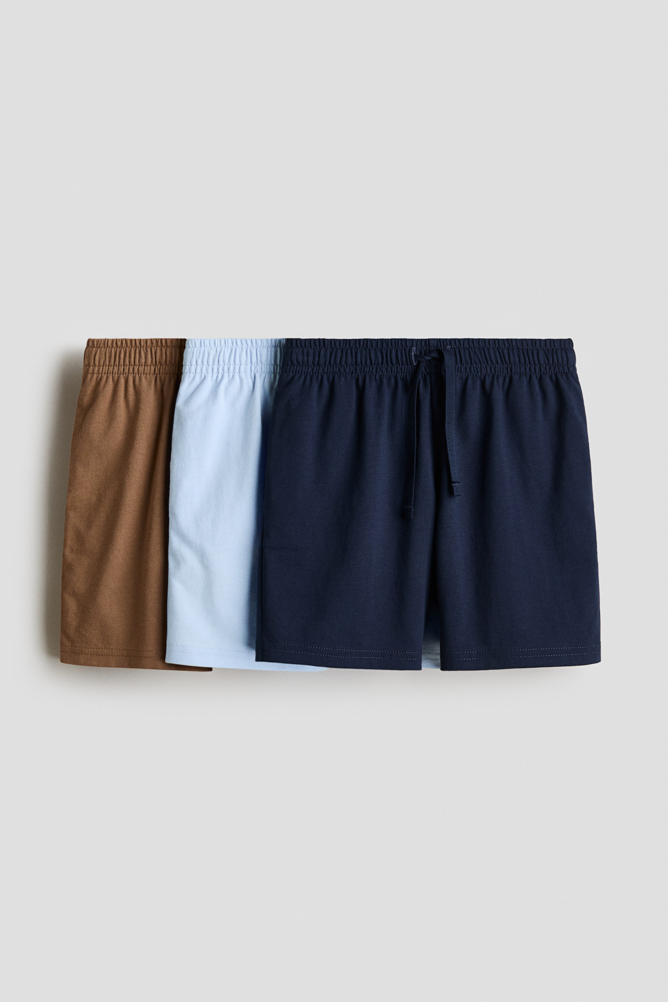 View larger image: Three pairs of knee-length shorts in soft cotton jersey are shown from the front, each with an elastic waistband. The navy pair also has a drawstring tie. Colors shown: brown, light blue, and navy.