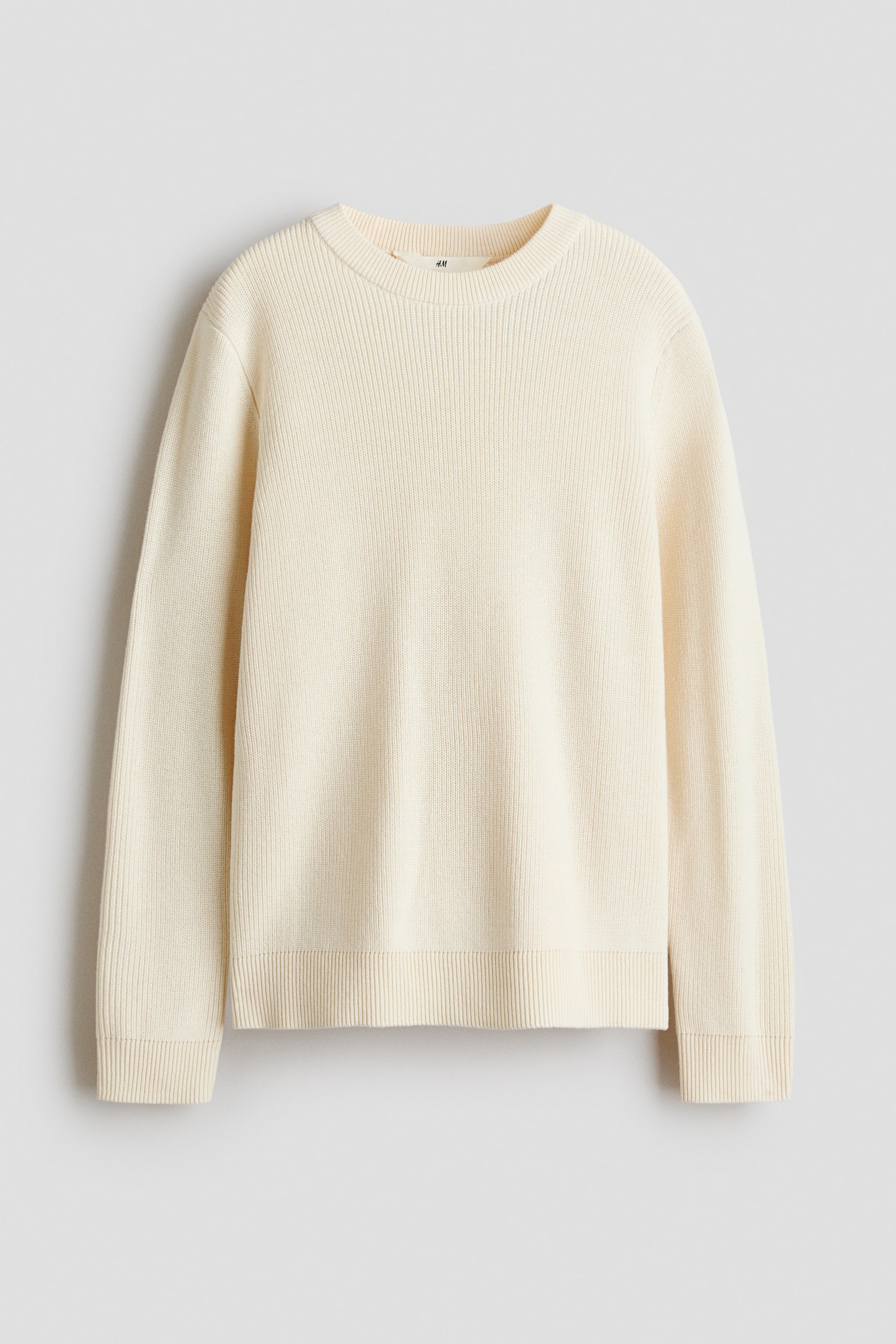 En cremefarvet sweater i ribstrik ses forfra med en rund halsudskÃ¦ring med ribkant og lange Ã¦rmer. Designet fremhÃ¦ver en blÃ¸d lodret ribstruktur med matchende ribmanchetter og ribkant forneden.