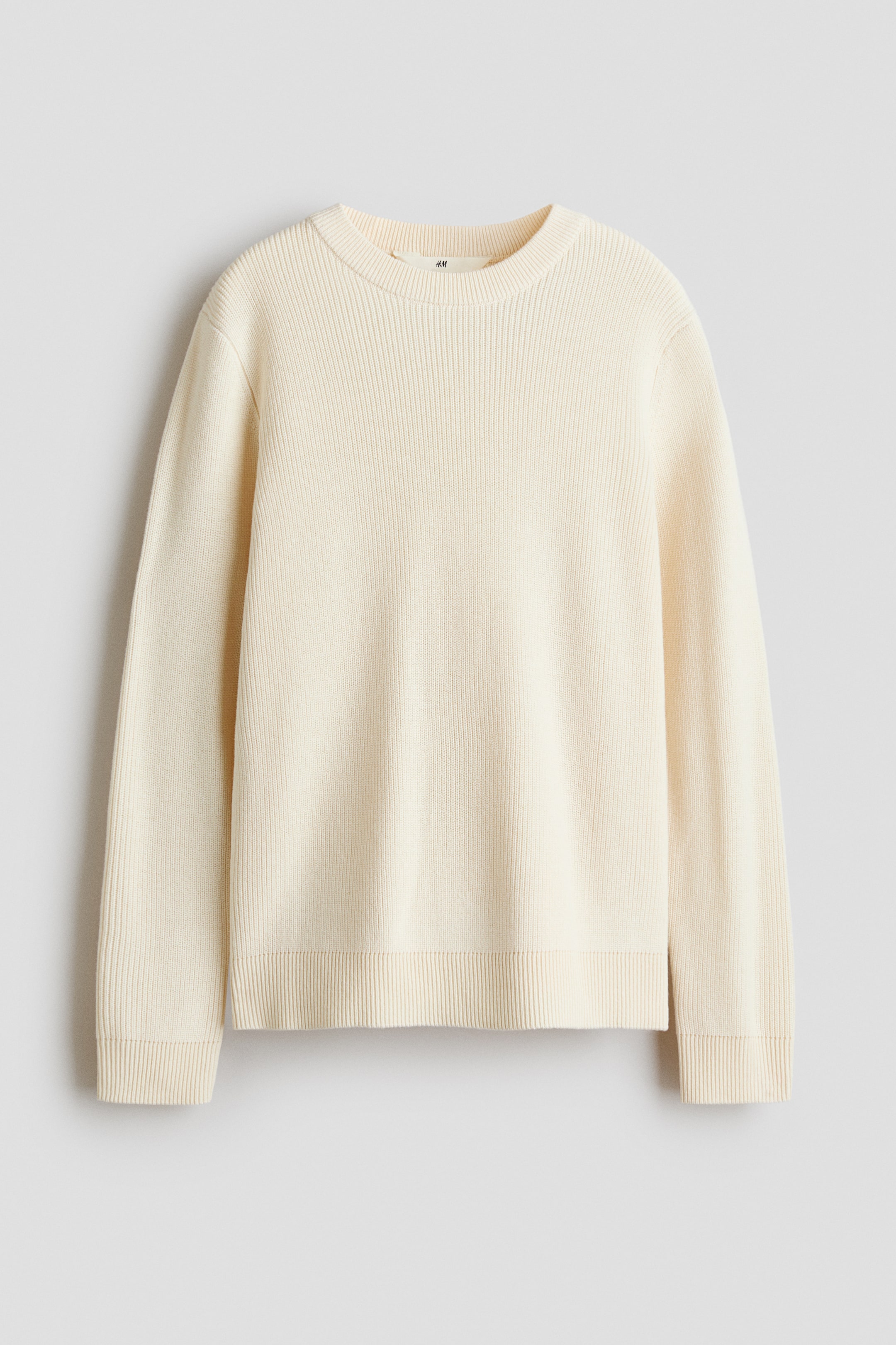 View larger image: A cream-colored, rib-knit sweater is shown from the front, featuring a round neckline with ribbed trim and long sleeves. The design highlights a soft vertical ribbed texture, with matching ribbed cuffs and a ribbed hem.