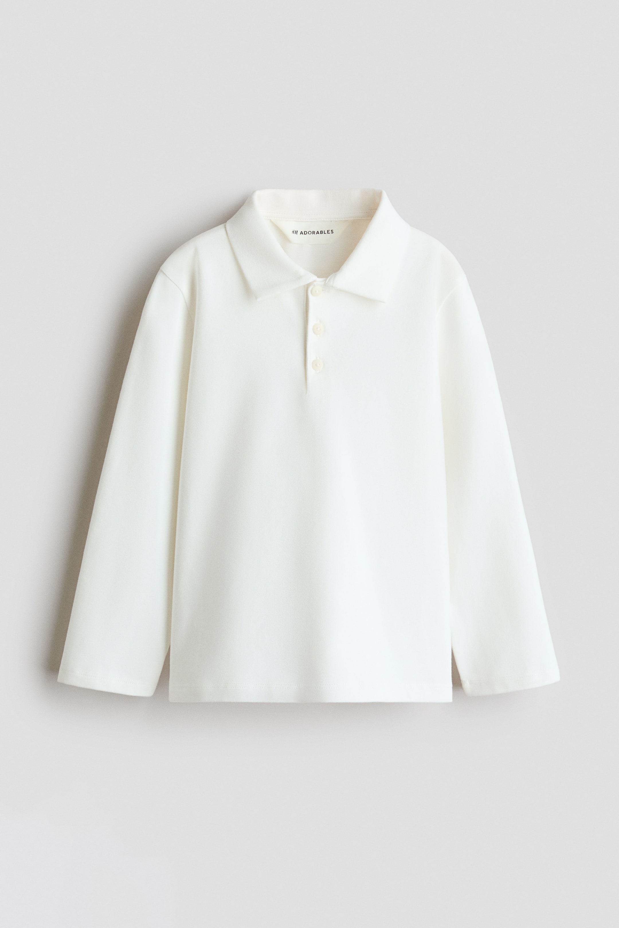Grotere afbeelding bekijken: Een poloshirt met lange mouwen in gebroken wit is van voren te zien, met een klassieke flat-knit kraag, een knoopsluiting met drie knopen en een rechte zoom.