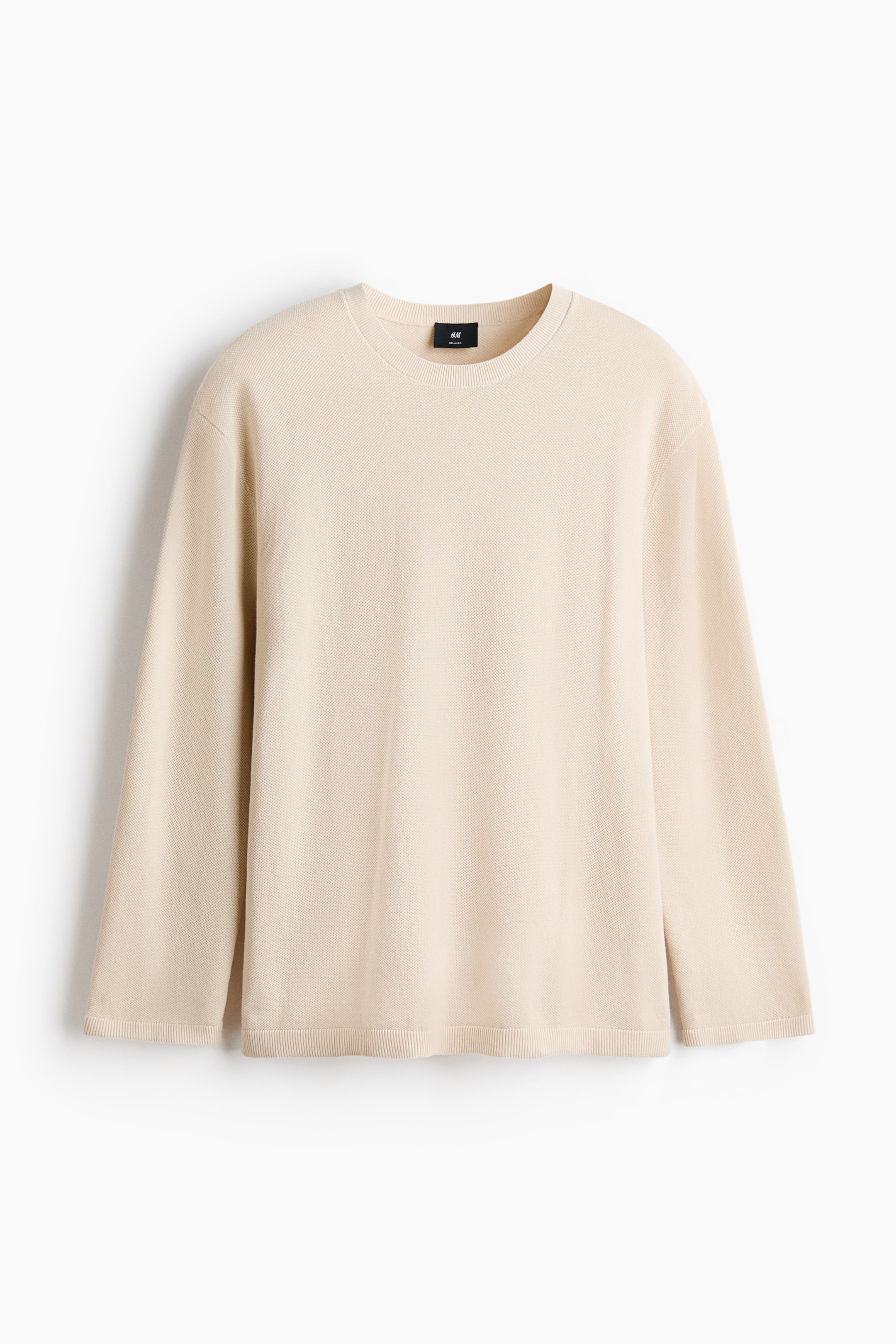 View larger image: A beige long-sleeved knit top is shown from the front, featuring a crew neck, long sleeves, and a fine textured knit. It is finished with ribbed cuffs and a ribbed hem.