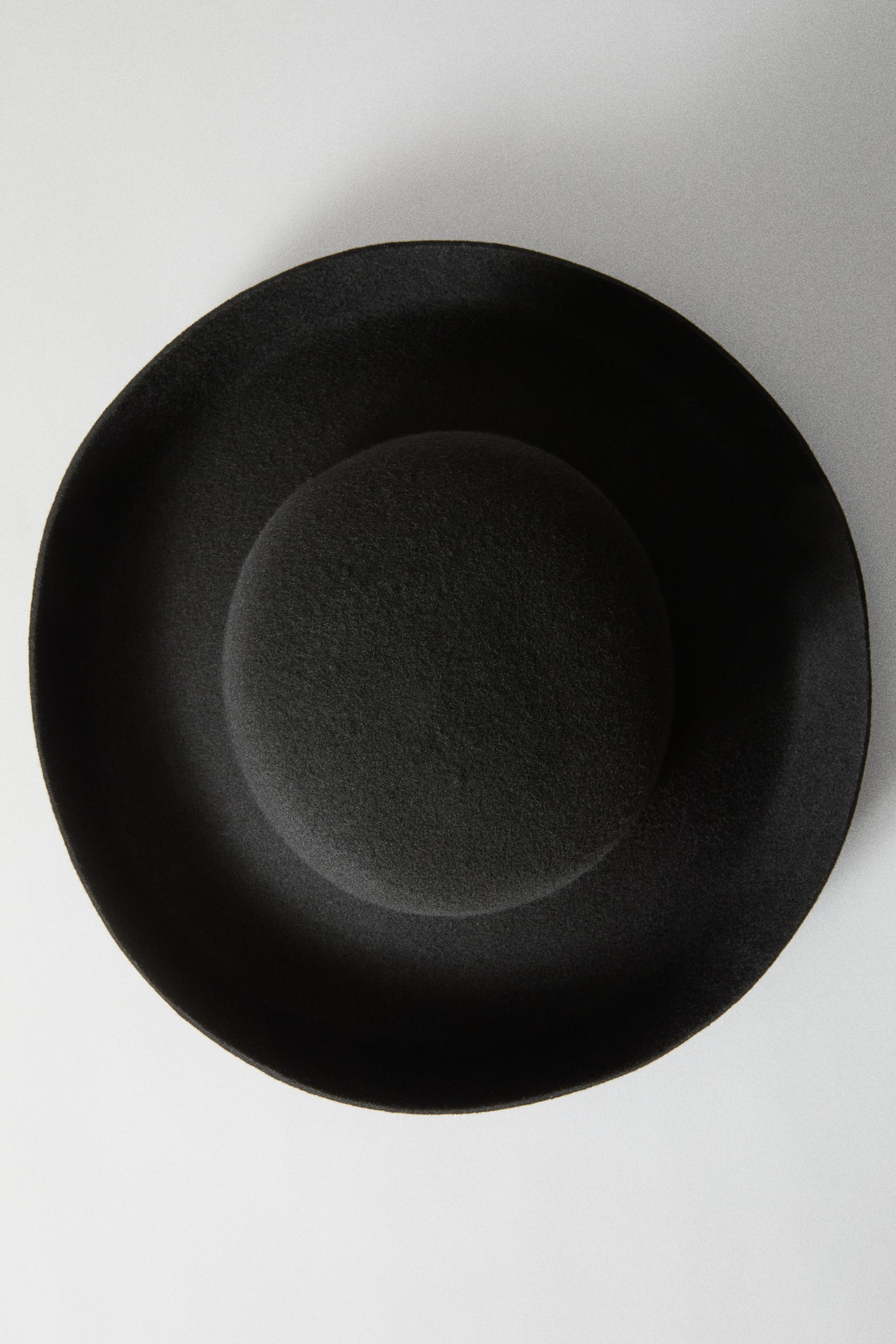 View larger image: A black felted wool hat is shown from a top-down view, featuring a rounded crown and a wide, circular brim.