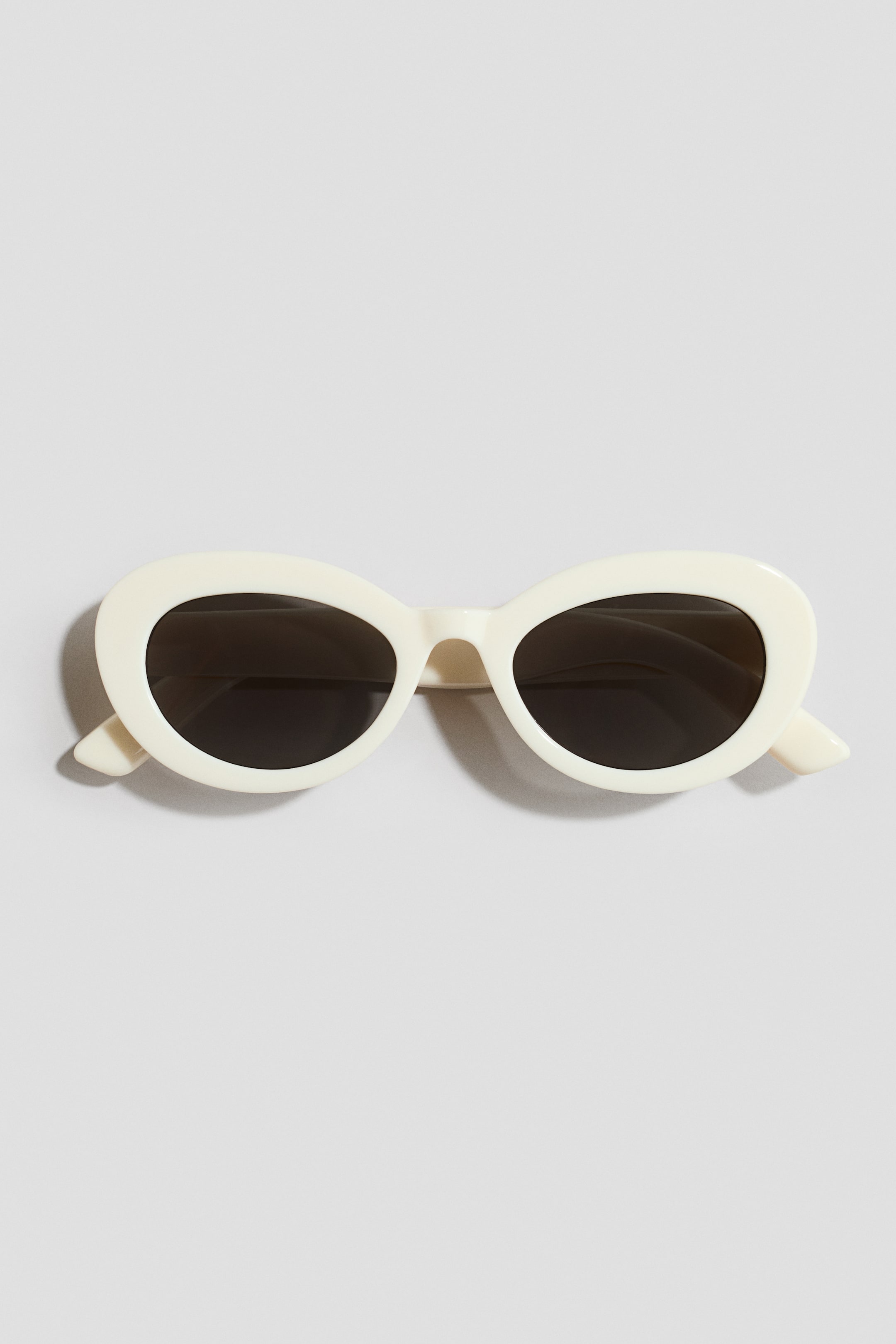View larger image: Plastic sunglasses are showcased frontally, boasting thick, off-white oval frames and dark tinted lenses.