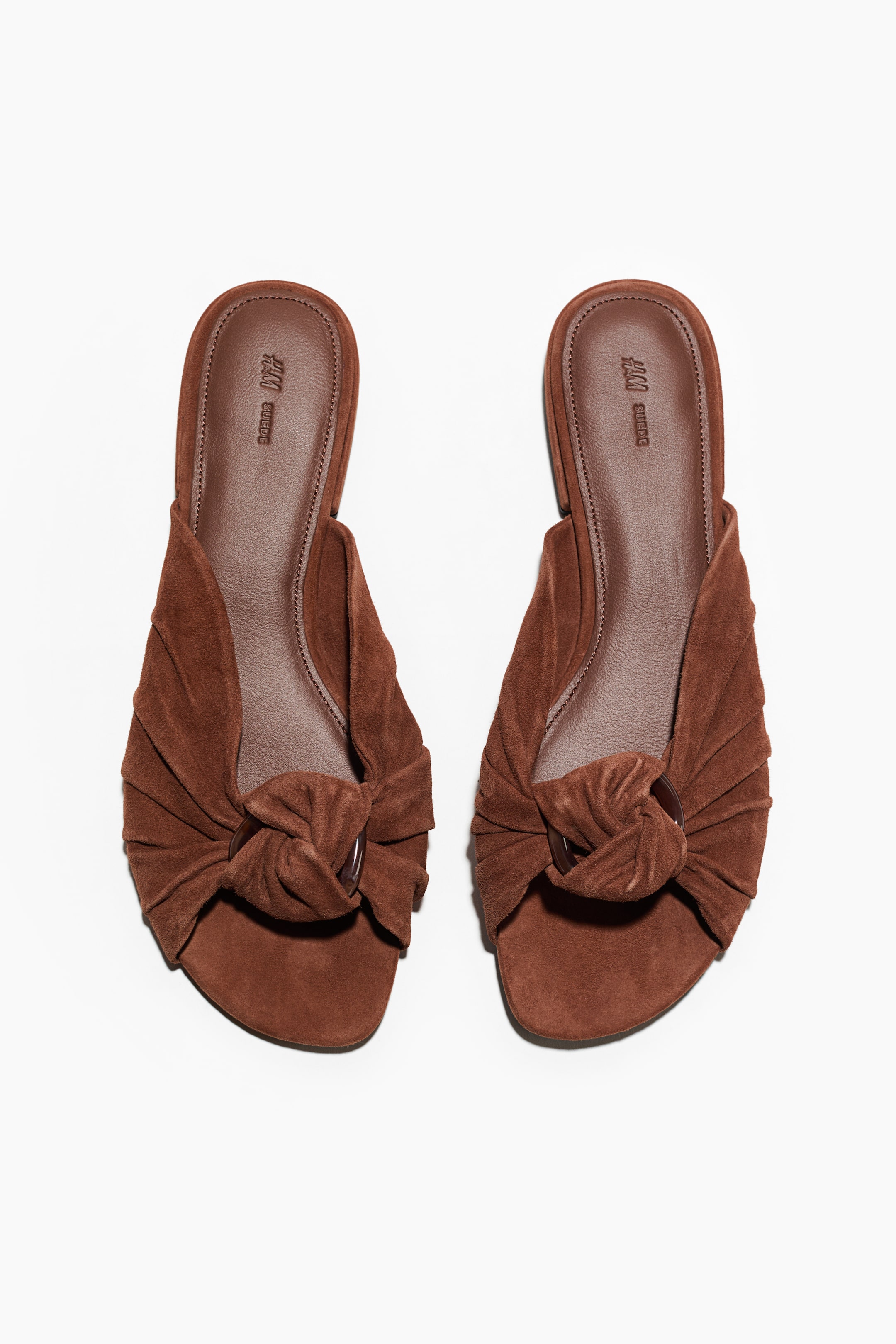 View larger image: Two brown suede sandals showcase a wide, ruched strap across the forefoot of each, gathering into a decorative knot at the centre. A dark ring-shaped buckle is integrated into the knot, and both sandals feature dark brown insoles.